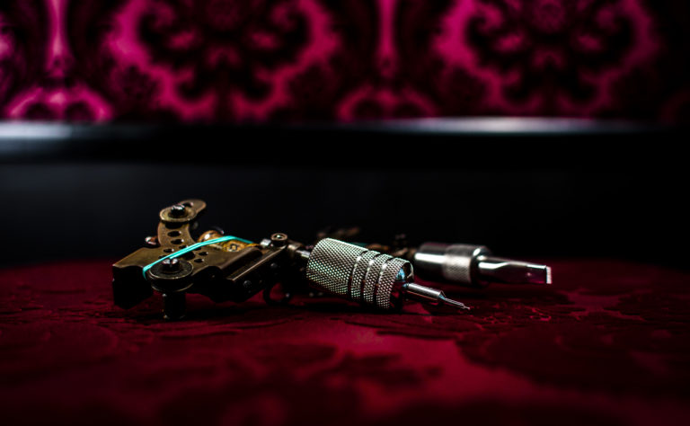 Coil tattoo machine fitted with a steel grip, resting on red damask fabric