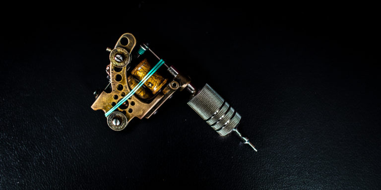 A custom brass and steel tattoo machine on a dark work surface at Idle Hands Tattoo Co.