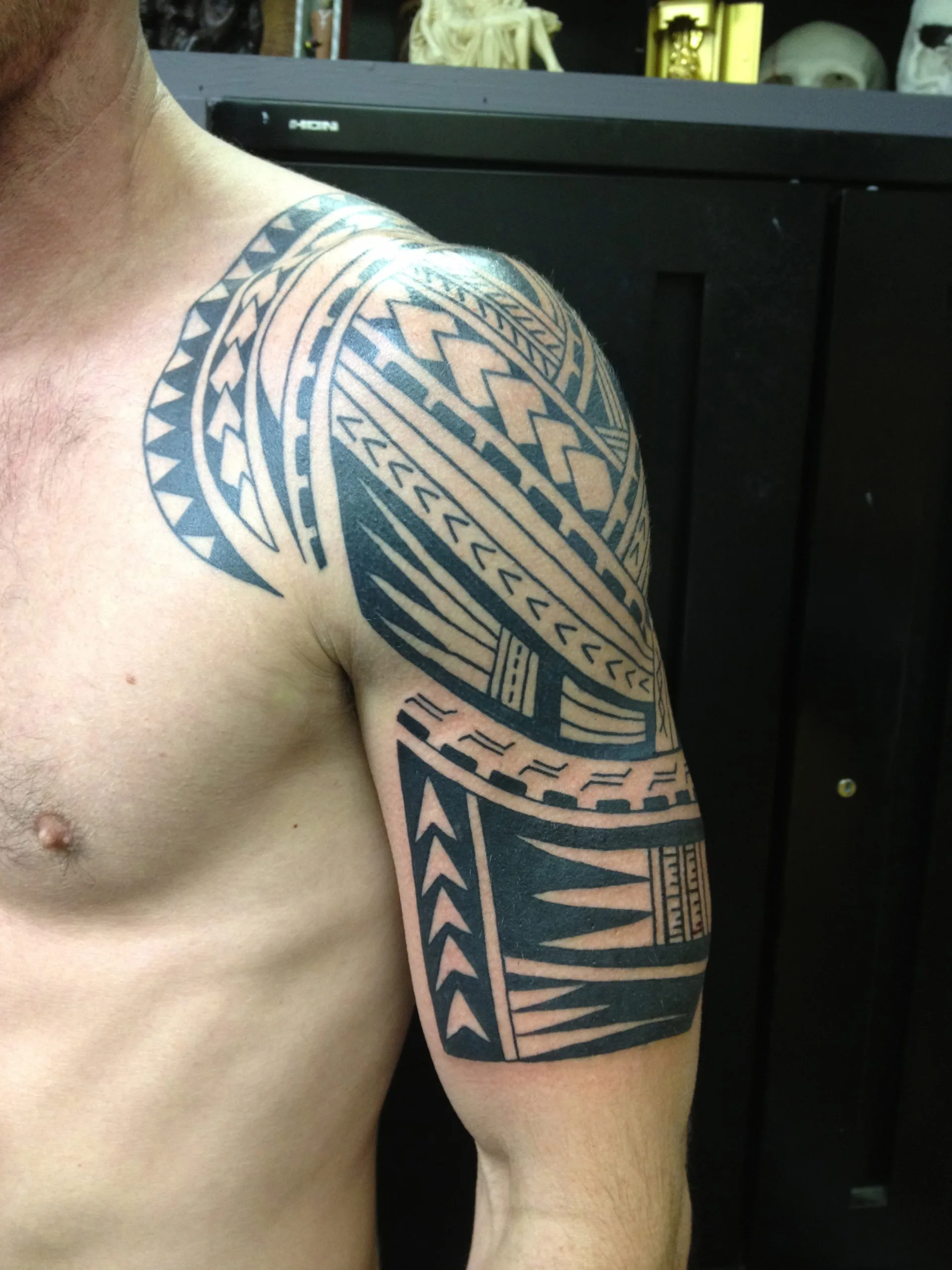 Black Polynesian-style tribal pattern covering the shoulder and upper arm with triangular and wave shapes