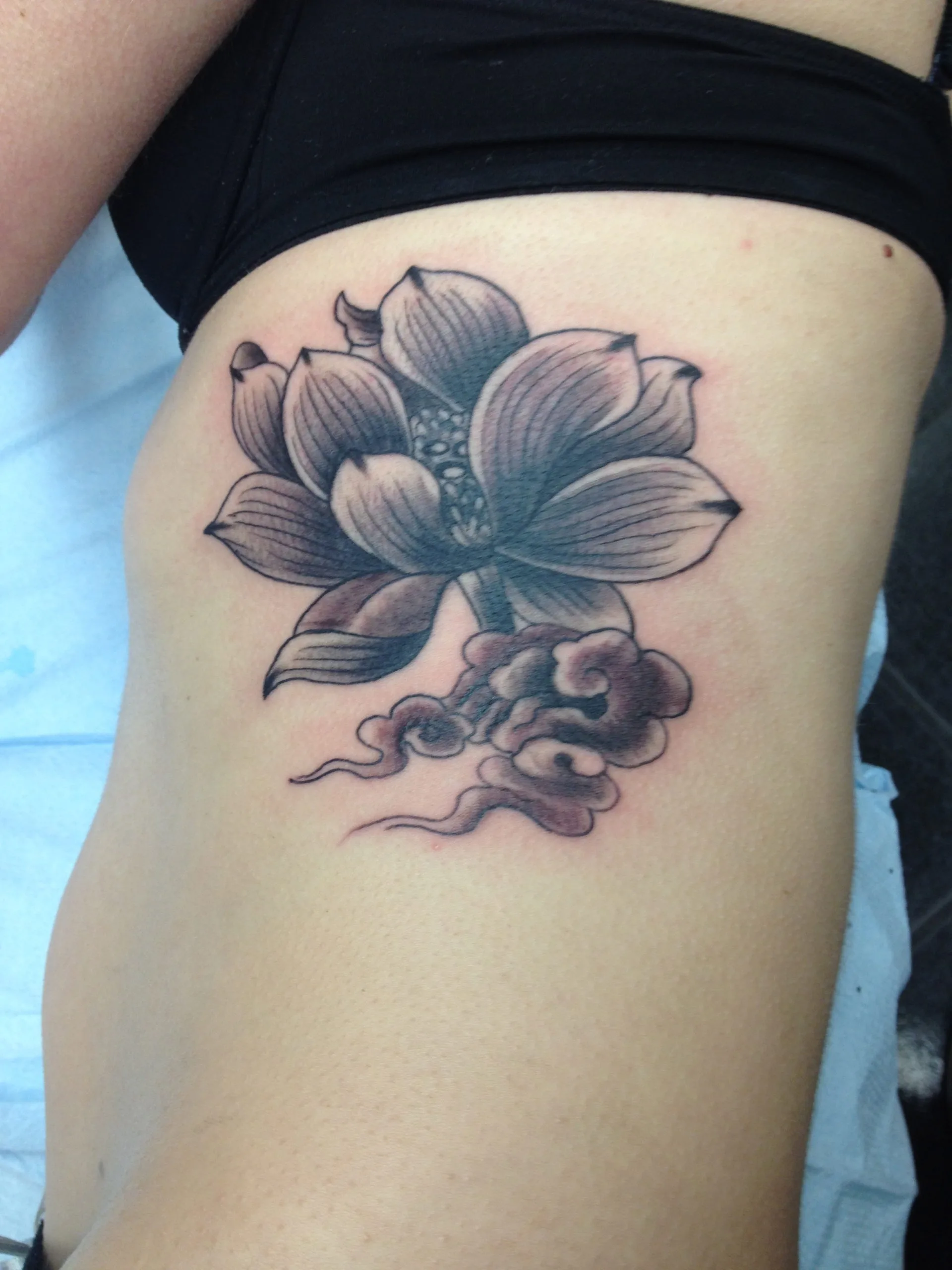 Black and grey lotus flower with a curling smoke-like design beneath it on the ribcage