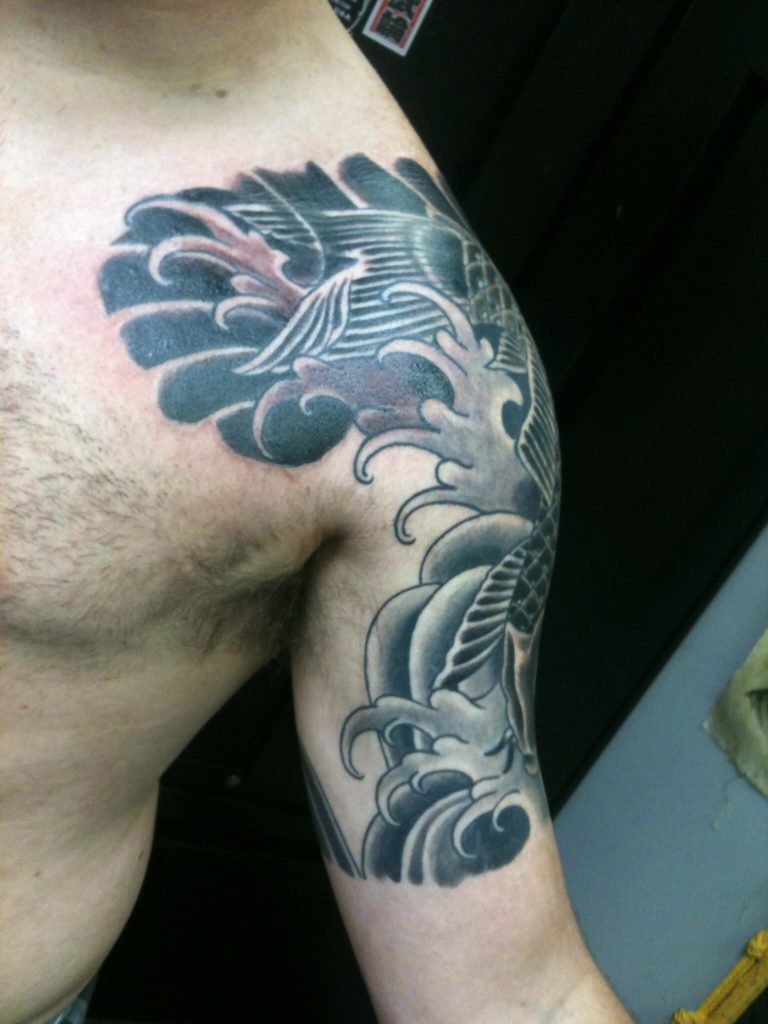 Black and grey wave and wing design spanning the chest, shoulder, and upper arm