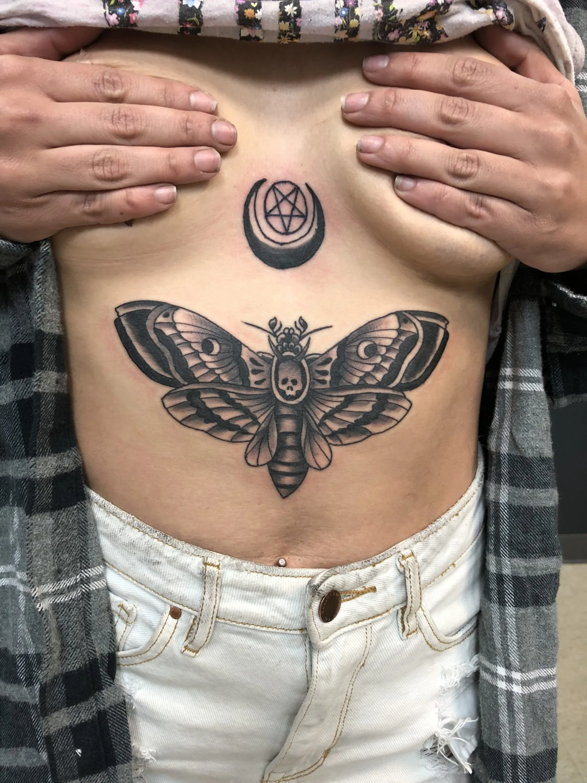 Black and grey moth beneath a crescent moon and pentagram, tattooed on the stomach