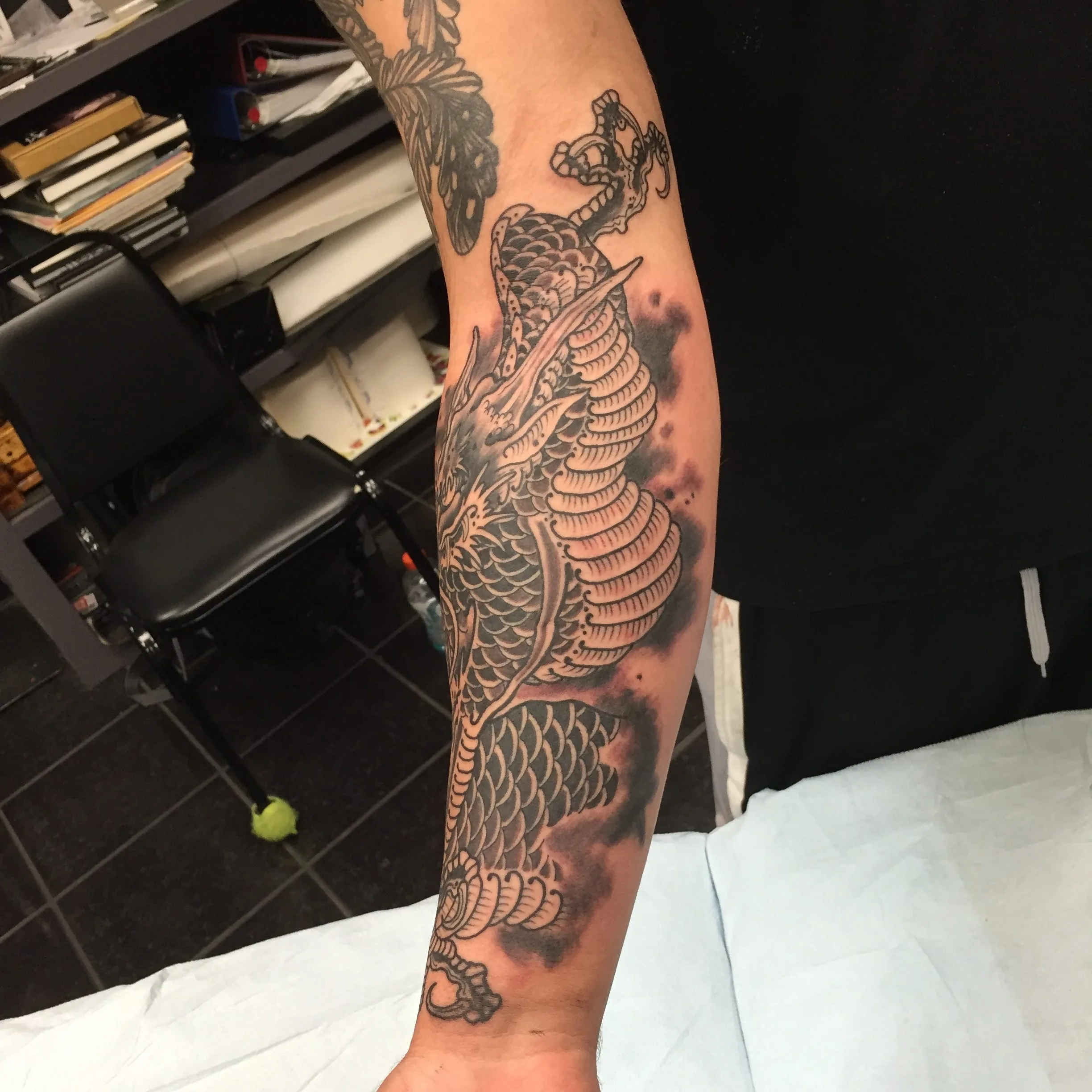Black and grey dragon with detailed scales and clouds on a forearm
