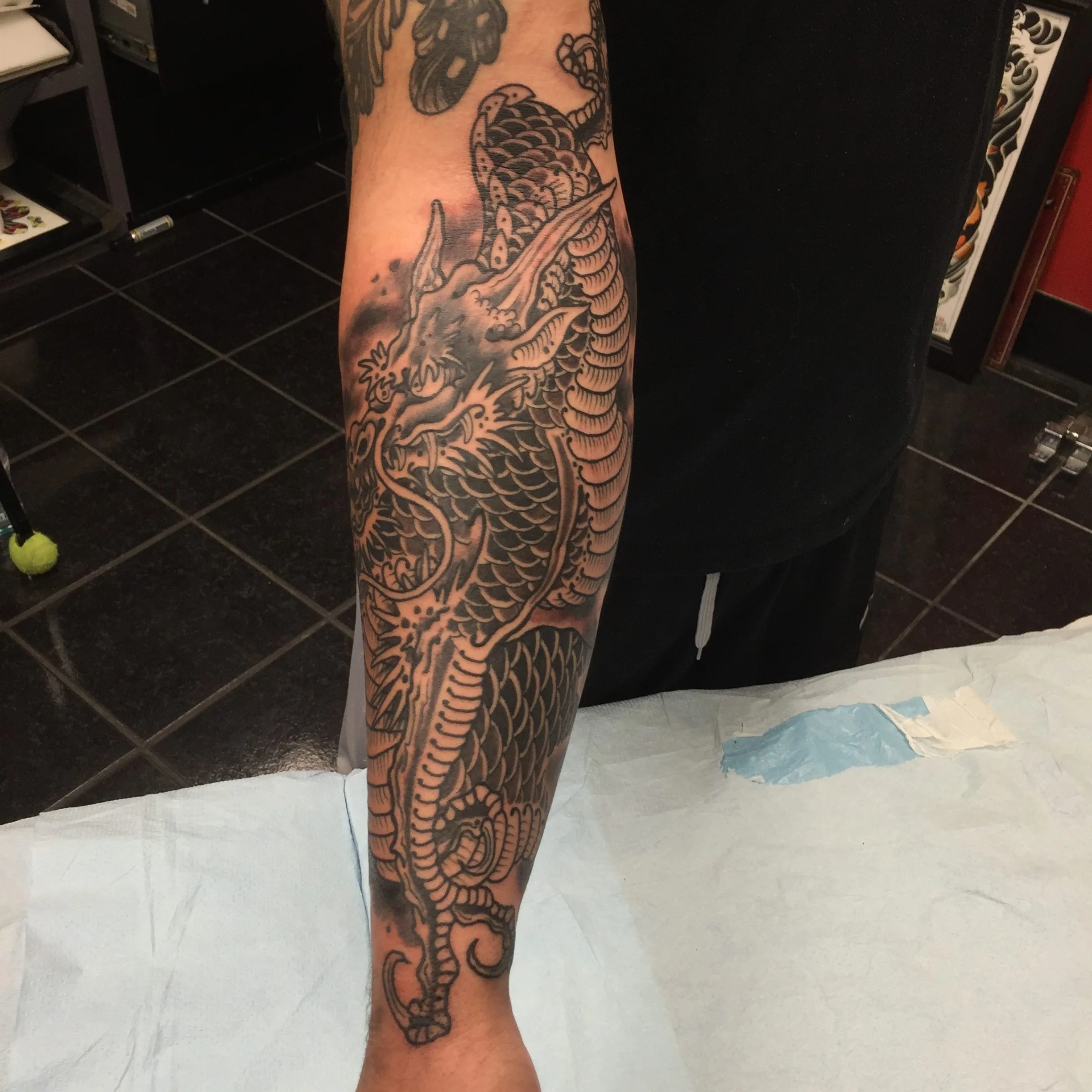 Black and grey forearm tattoo of a dragon head with detailed scales