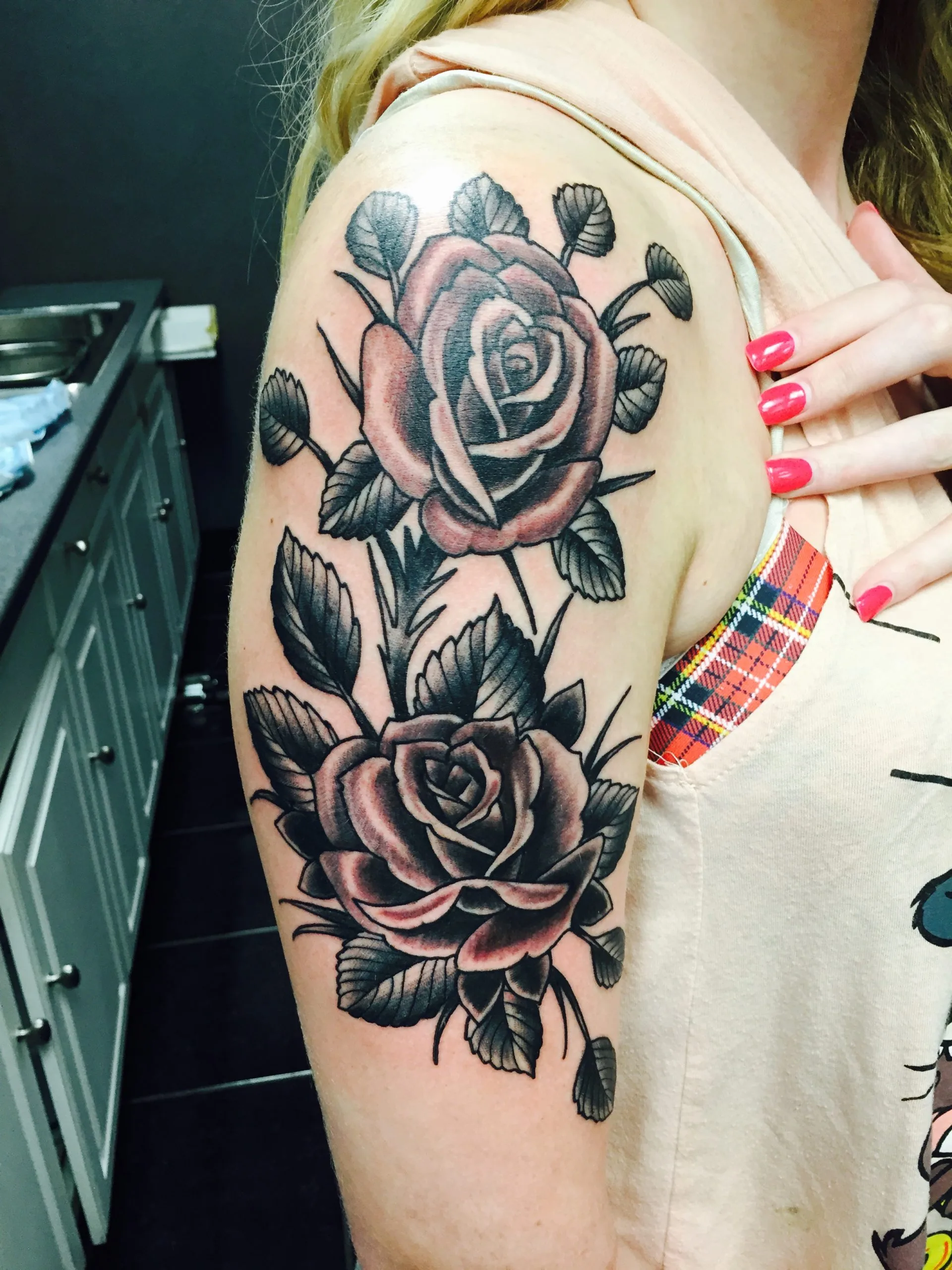 Two black and grey roses with foliage on the upper arm, seen from above the shoulder