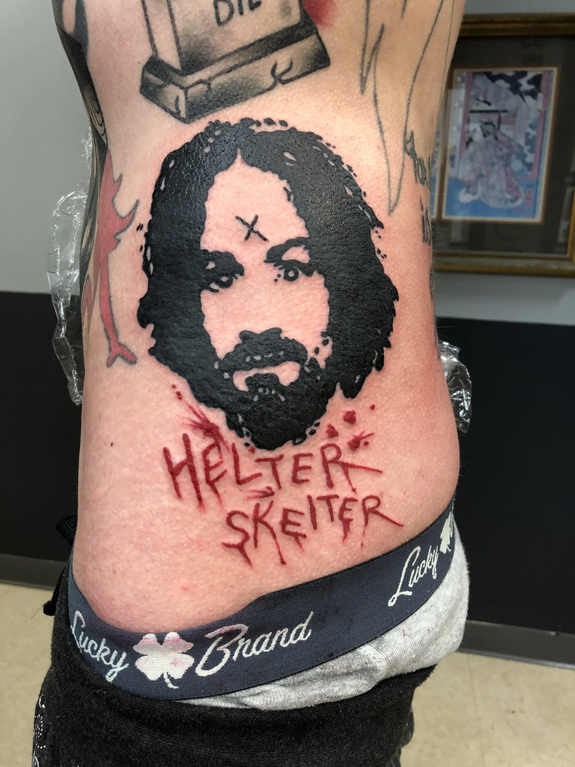 Black ink face portrait with an X marked on the forehead, red 'HELTER SKELTER' lettering below, on the ribs