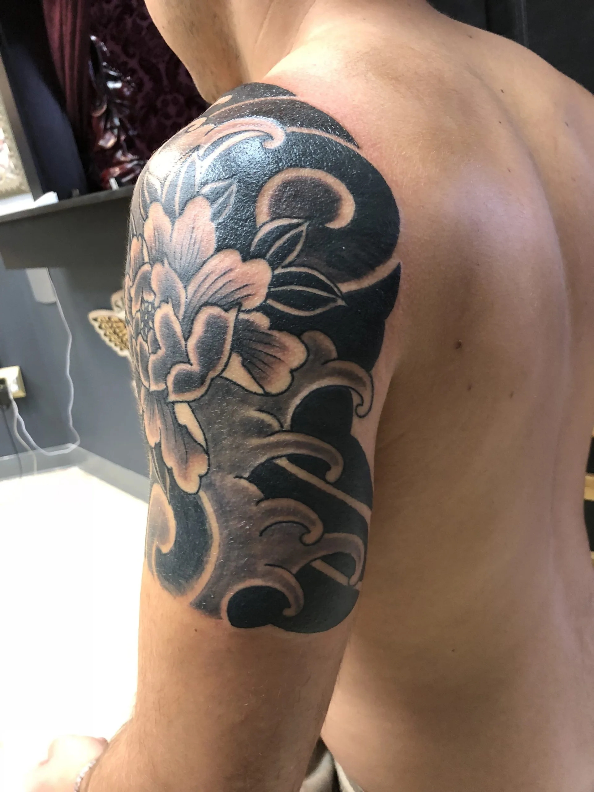 Black and grey peony flower with swirling wave scrollwork on the shoulder and upper arm