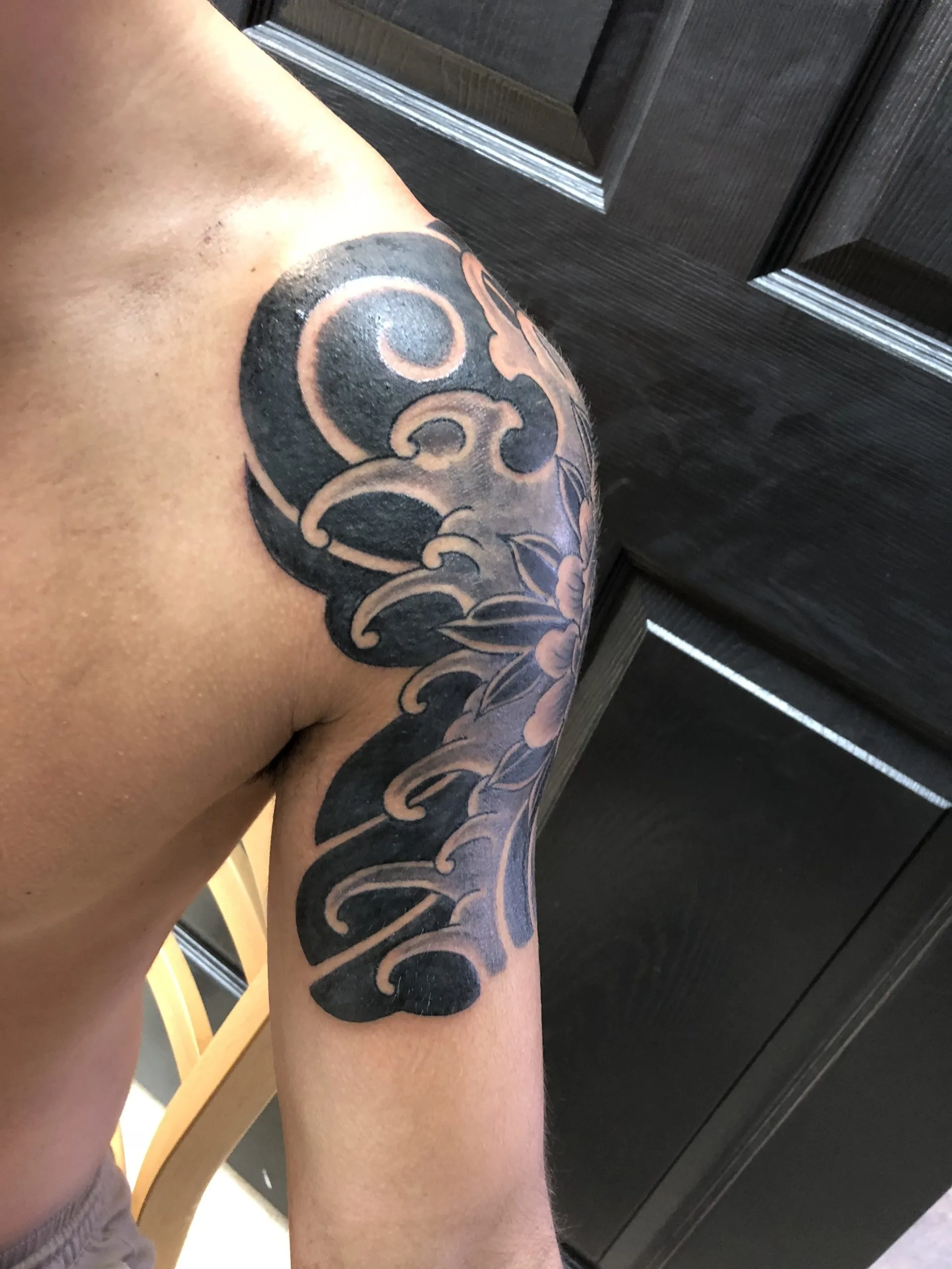 Black and grey wave scrollwork with a flower accent on the shoulder and upper arm