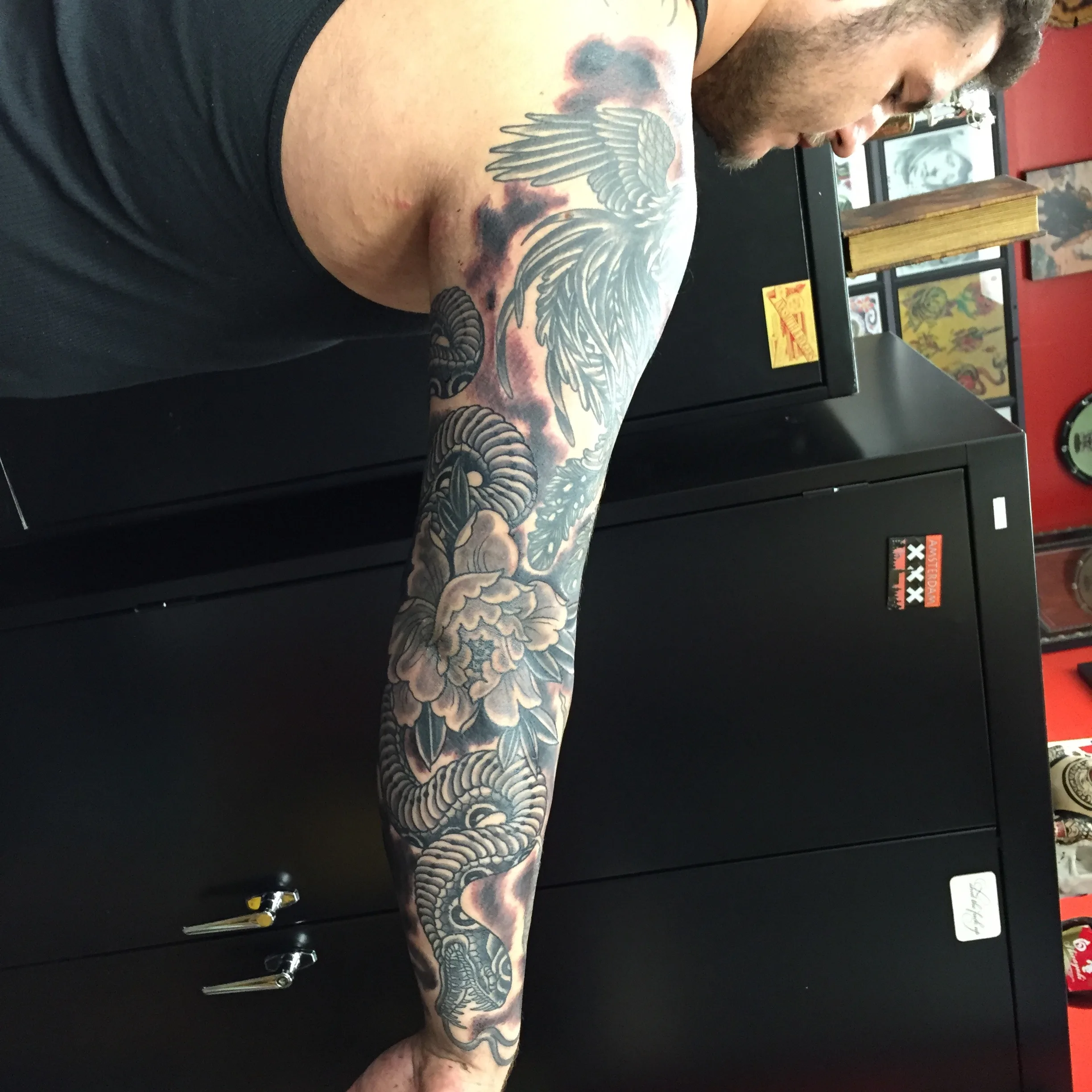 Black and grey full-arm sleeve with a wing design at the shoulder flowing into a large peony blossom down the arm