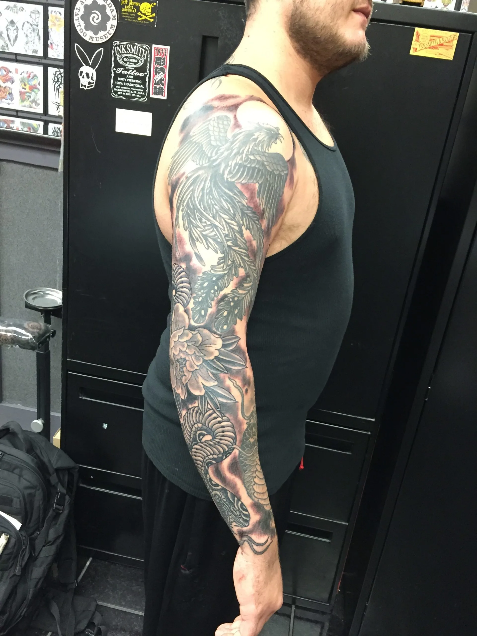 Full black and grey sleeve with a phoenix-like bird above a peony and swirling clouds
