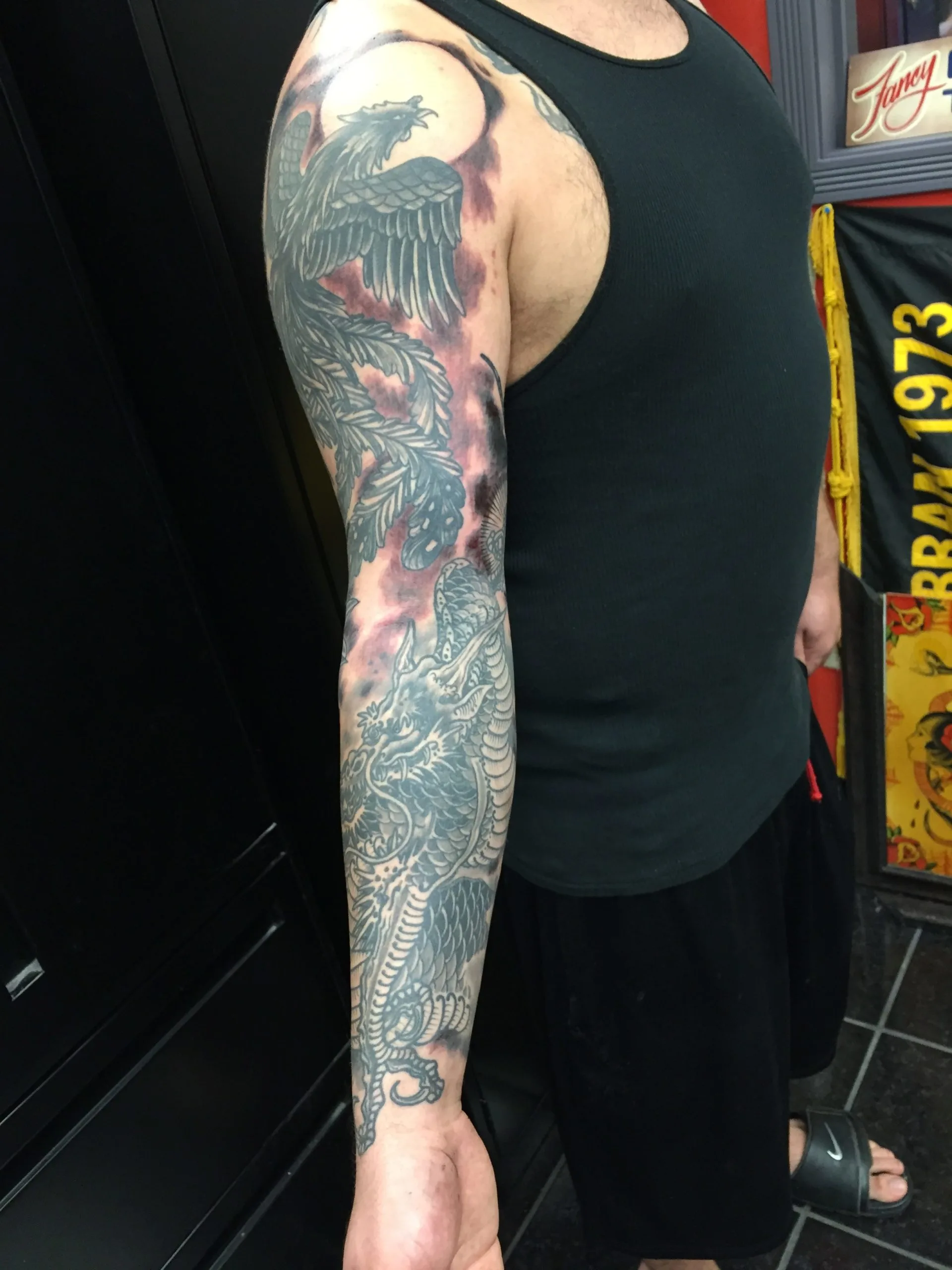 Black and grey full arm sleeve with a phoenix at the shoulder and dragon scales down to the wrist, red background