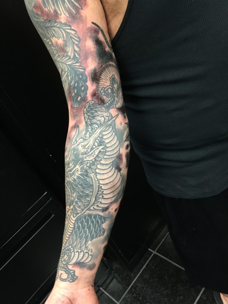 Black and grey dragon with feathered cloud shading, running the full arm from shoulder to wrist