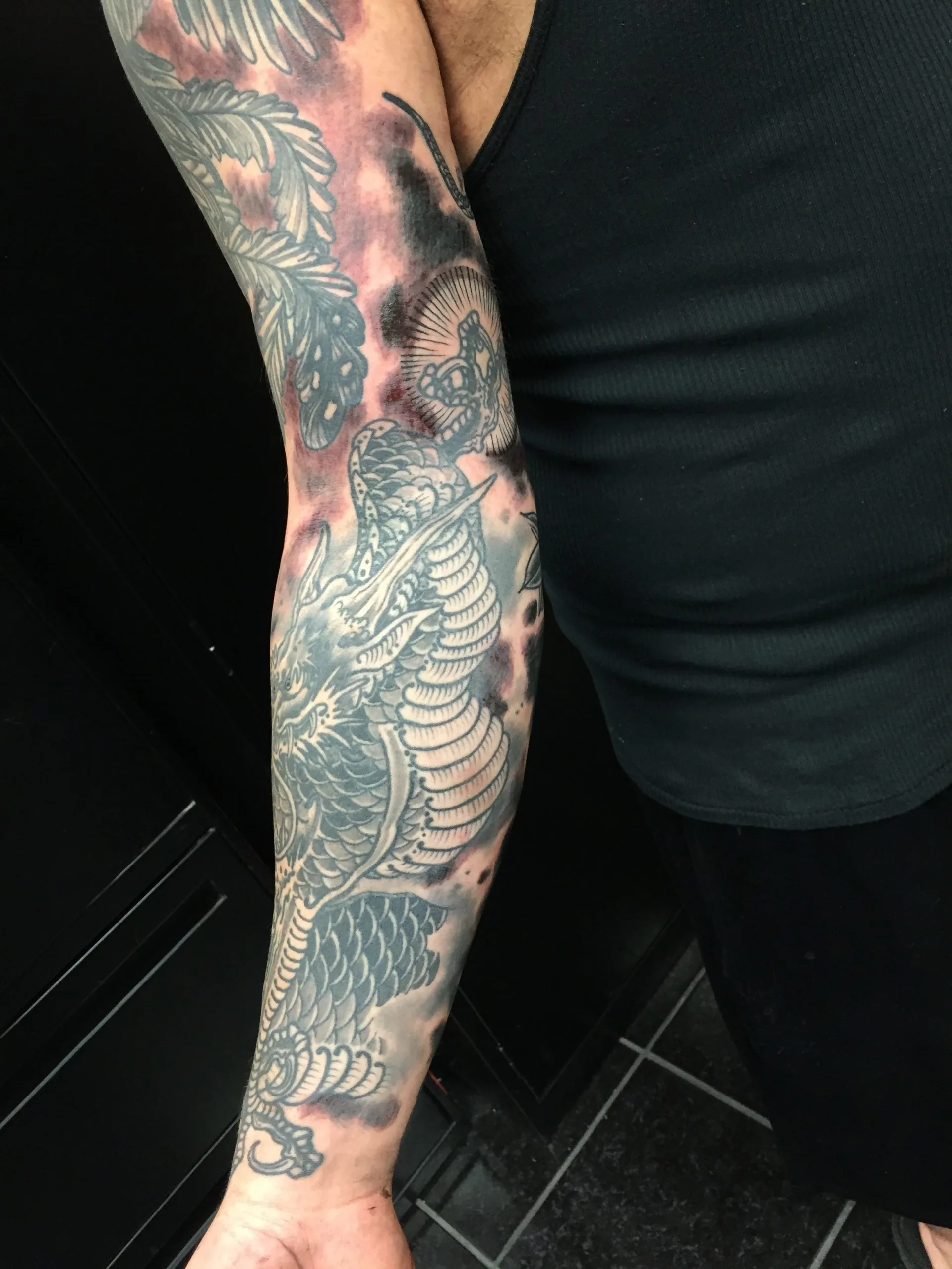 Black and grey dragon with feathered cloud shading, running the full arm from shoulder to wrist