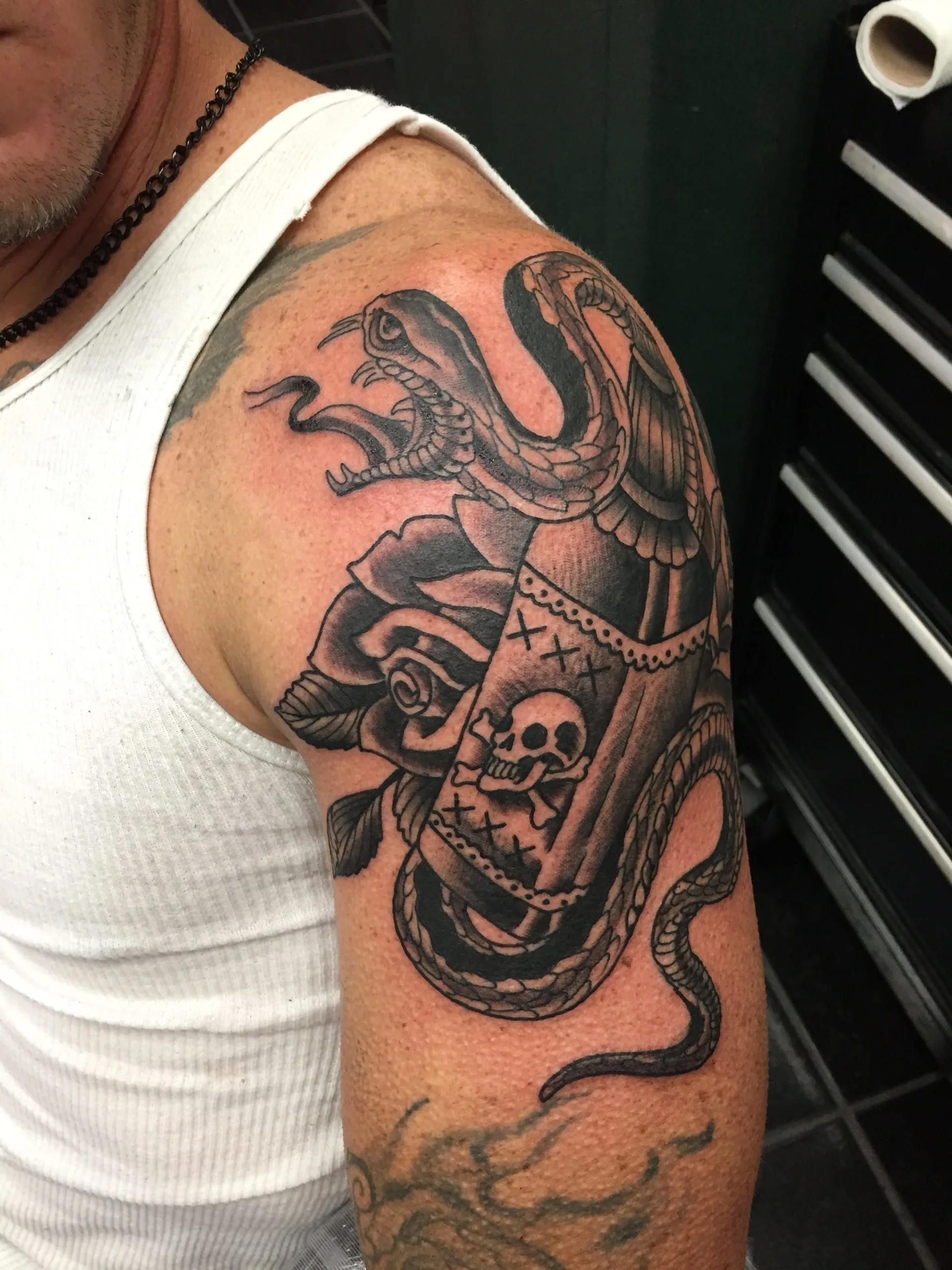 Black and grey shoulder and upper arm tattoo of a snake coiled around a rose and a skull and crossbones banner