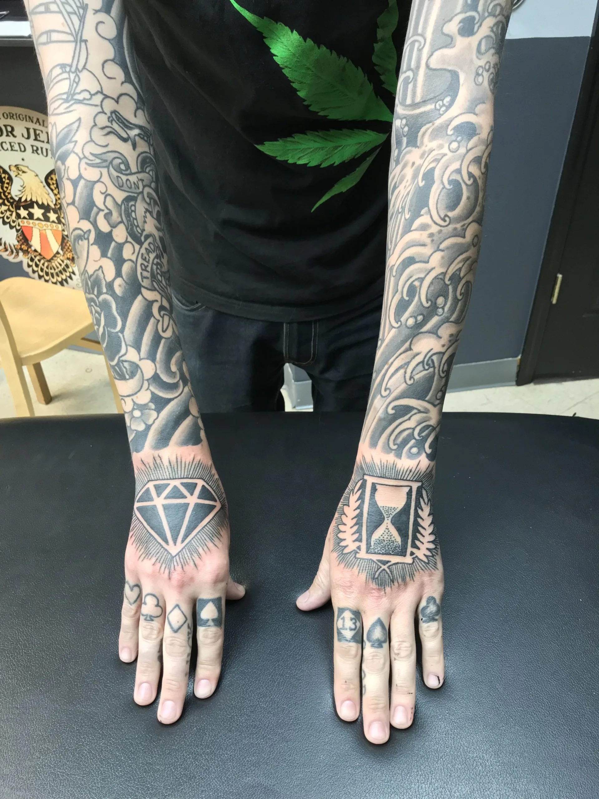 Black and grey wave-pattern forearms with diamond, hourglass, and playing-card tattoos across both hands