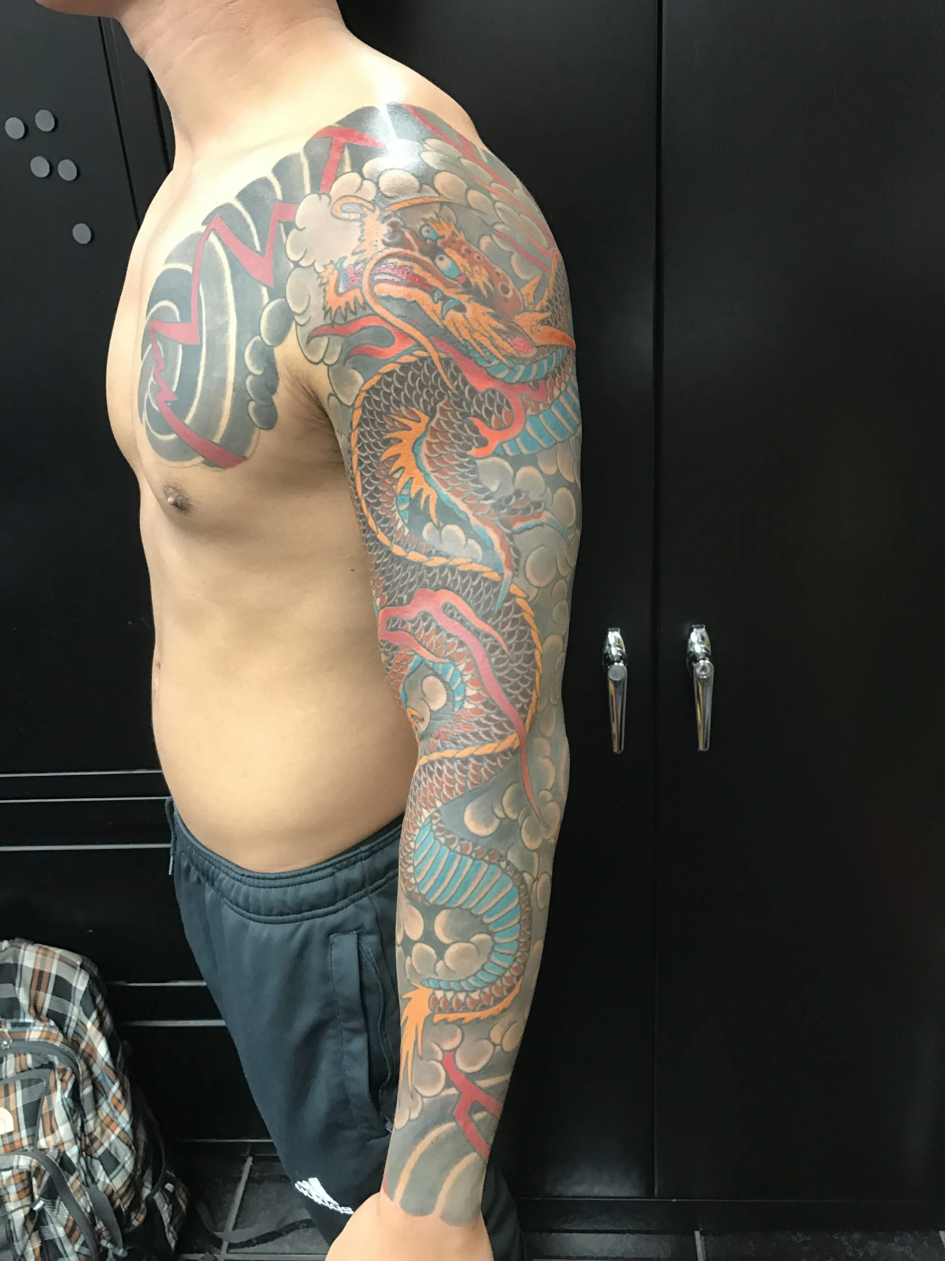 Front view of a colour Japanese dragon sleeve, the dragon's teal belly winding through grey clouds and red wind bars