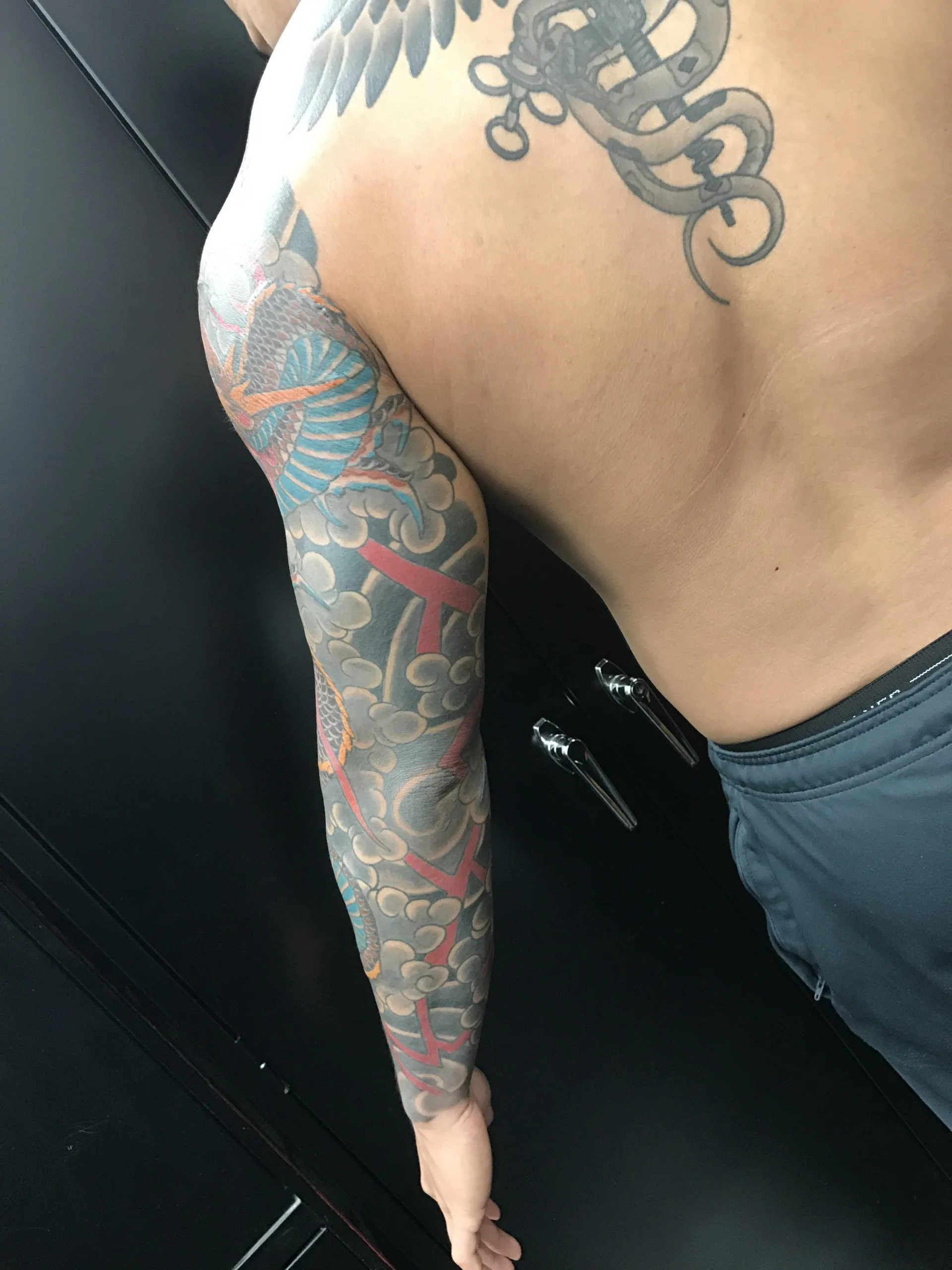 Back view of a colour Japanese dragon sleeve across the shoulder, with unfinished black outline work on the upper back
