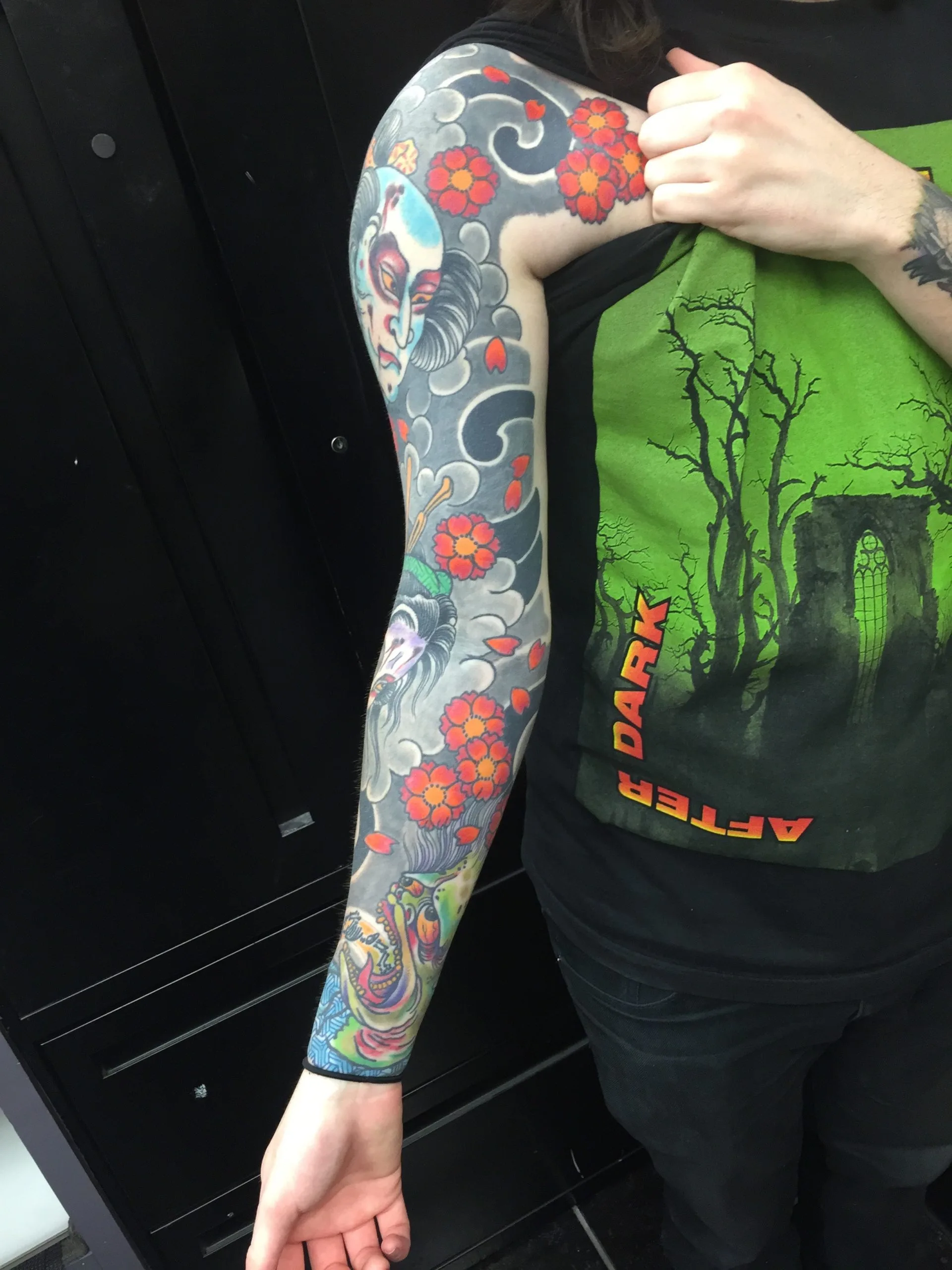 Colour Japanese sleeve of a woman's face and red blossoms over grey wind bars, running the full length of the arm