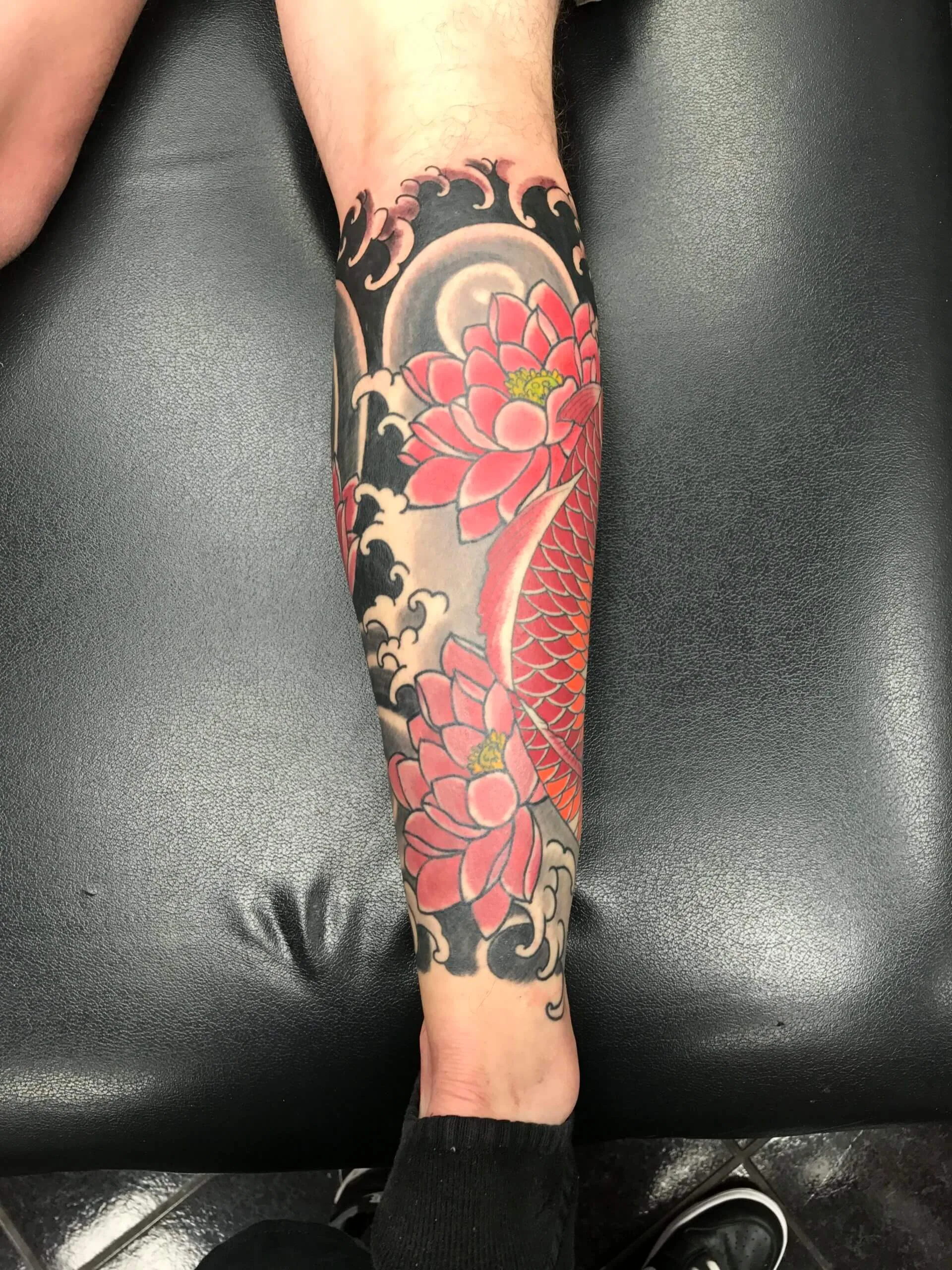 Red koi swimming past pink chrysanthemums on a lower leg, over black and grey waves