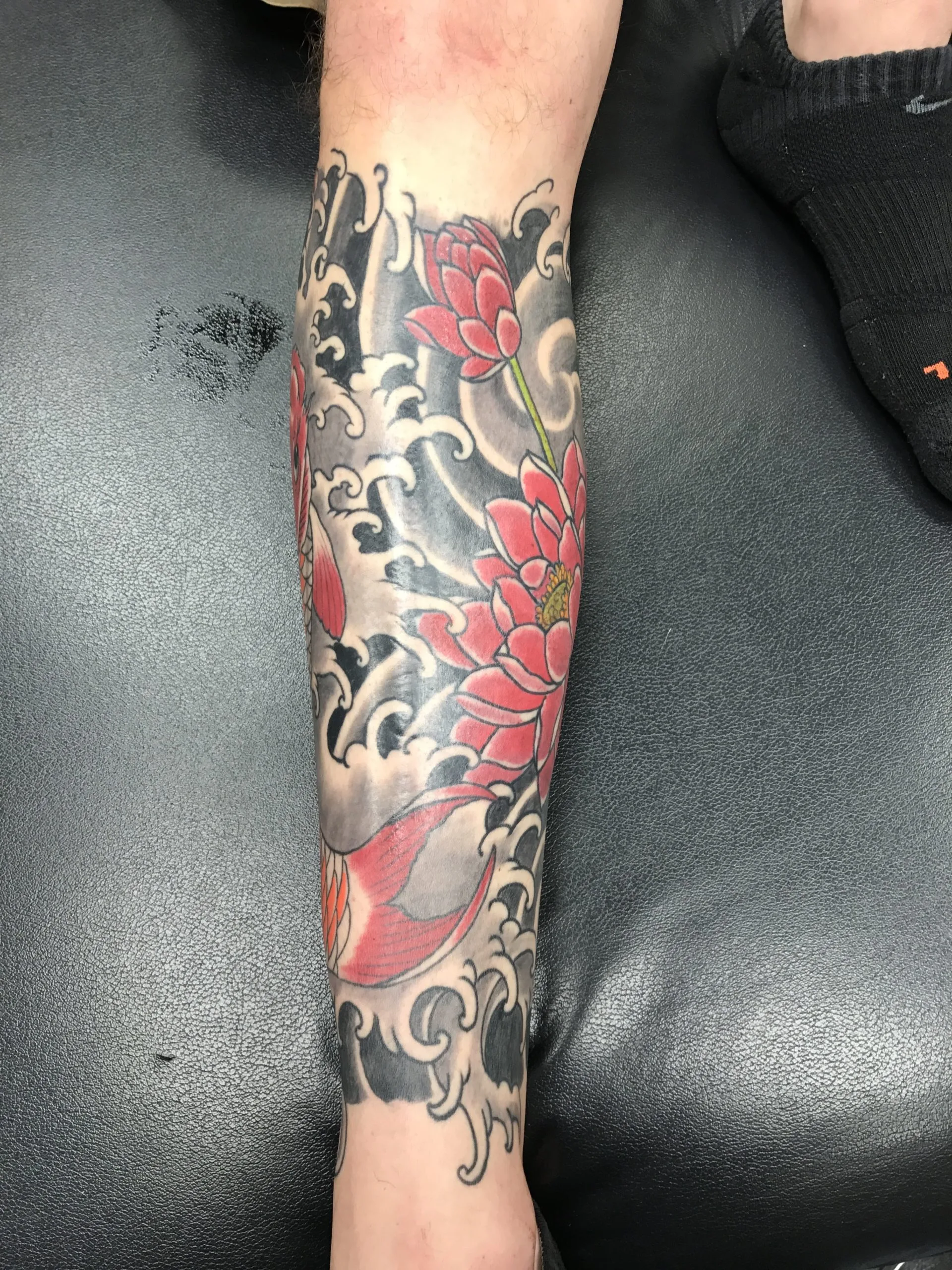 Red chrysanthemums and the tail of a koi wrapping a lower leg, over black and grey waves