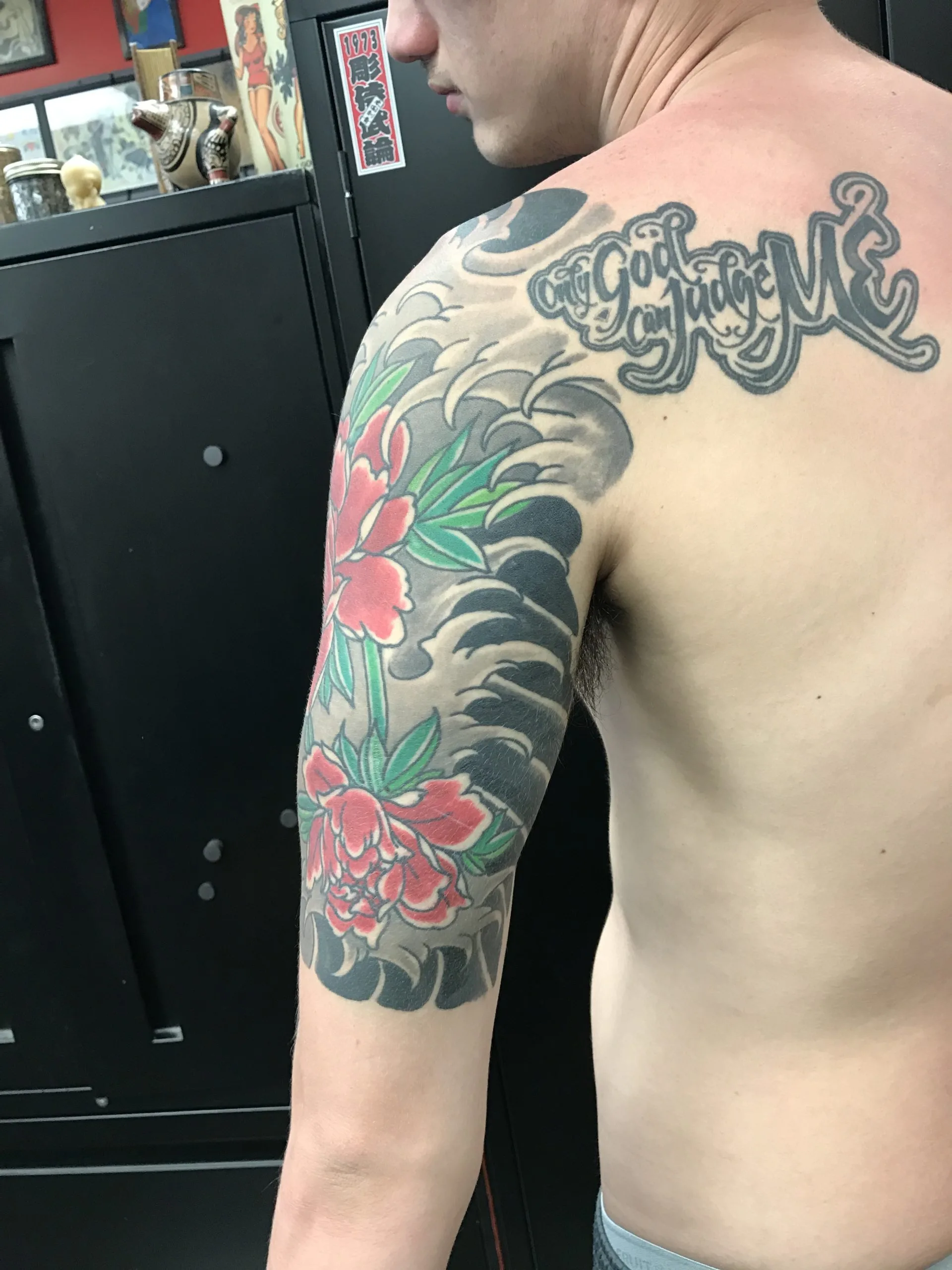 Back view of a red peony half sleeve over grey waves, with script lettering across the shoulder blade