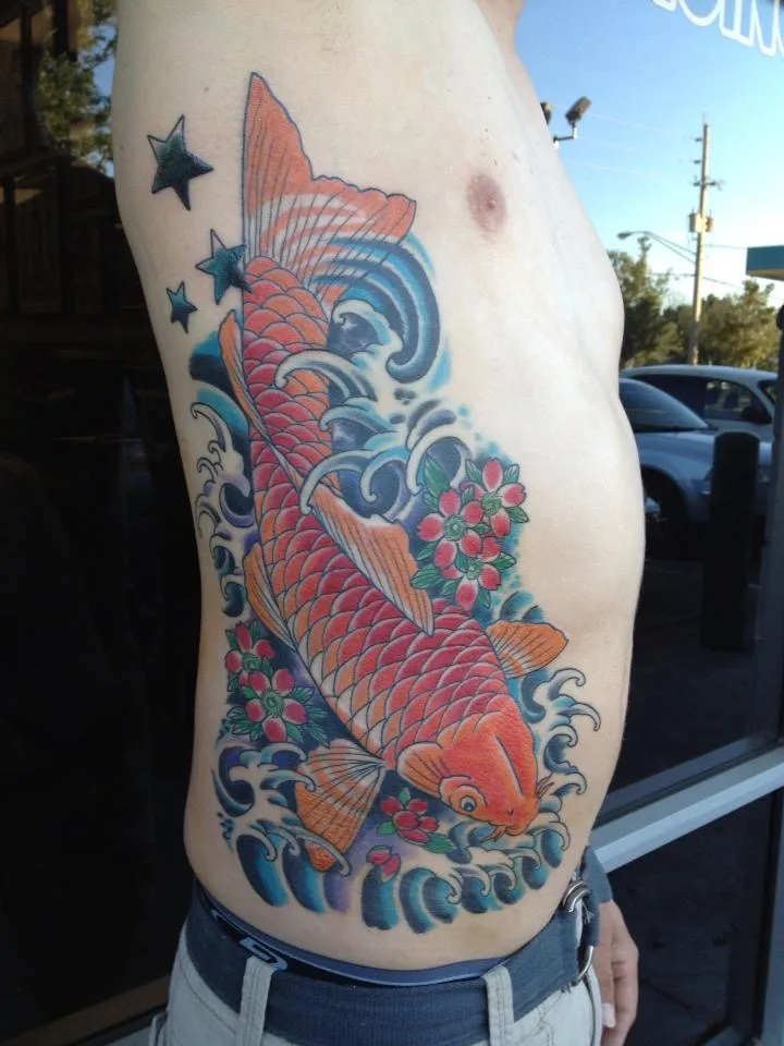 Large orange koi across the ribs and side, swimming through blue waves with red flowers and blue stars