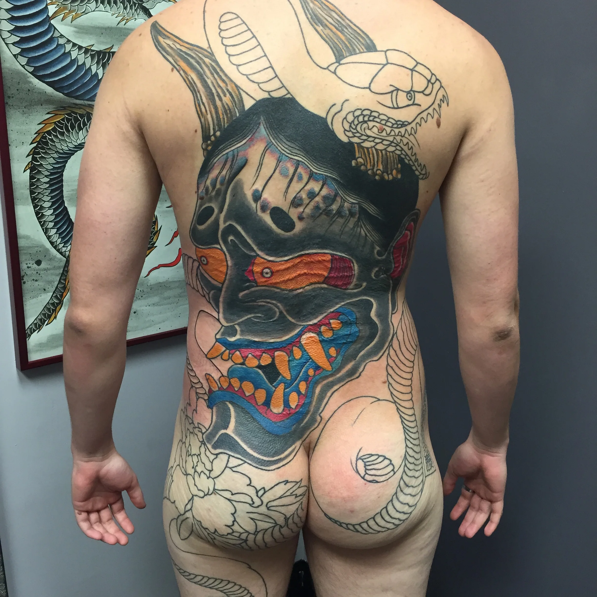 Large dark horned mask back piece with orange teeth and a blue mouth, still in progress with outline work on the lower back