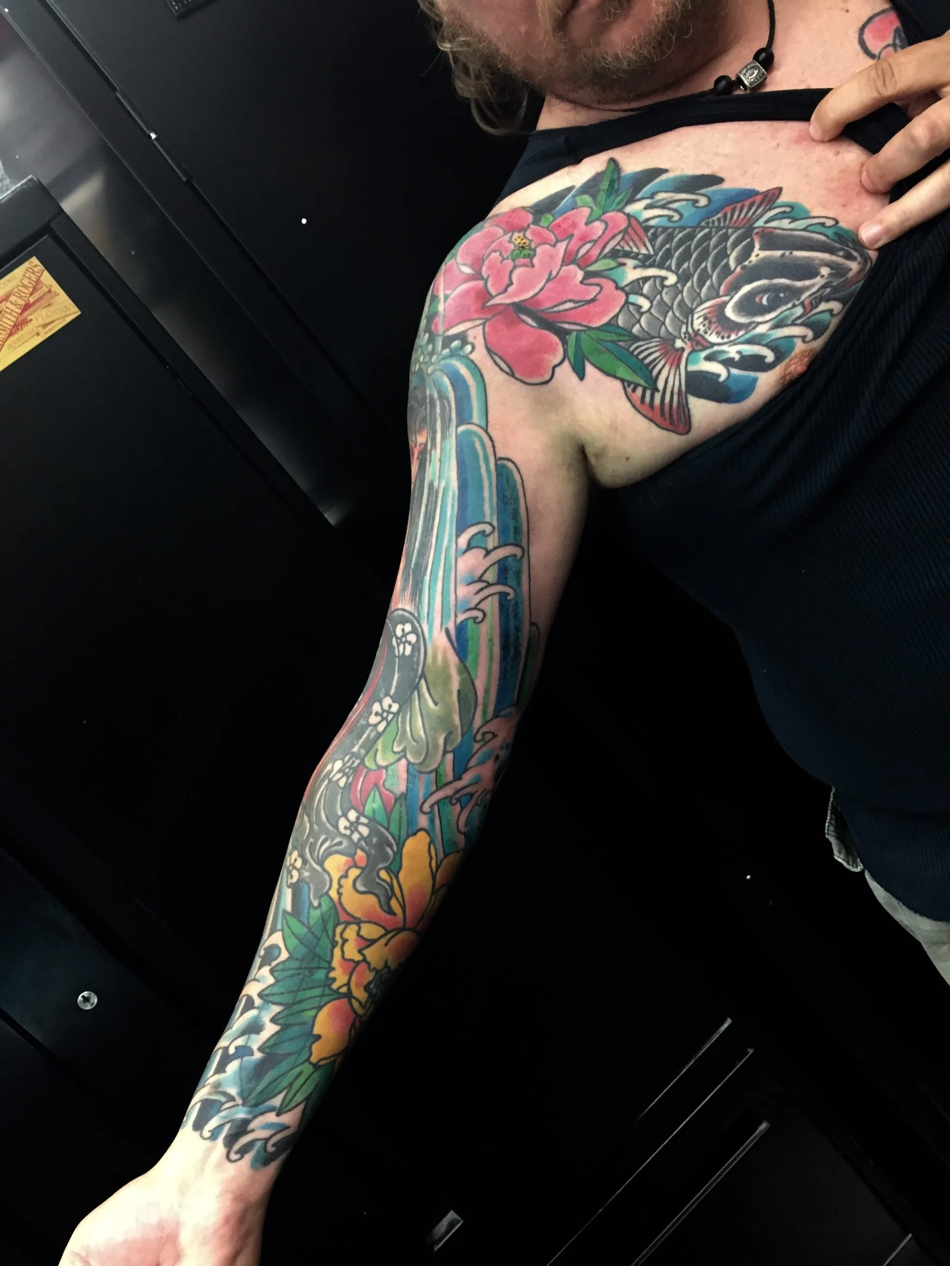 Colour Japanese full sleeve with a dark koi and pink peony at the shoulder, a blue waterfall down the arm and a yellow chrysanthemum at the wrist