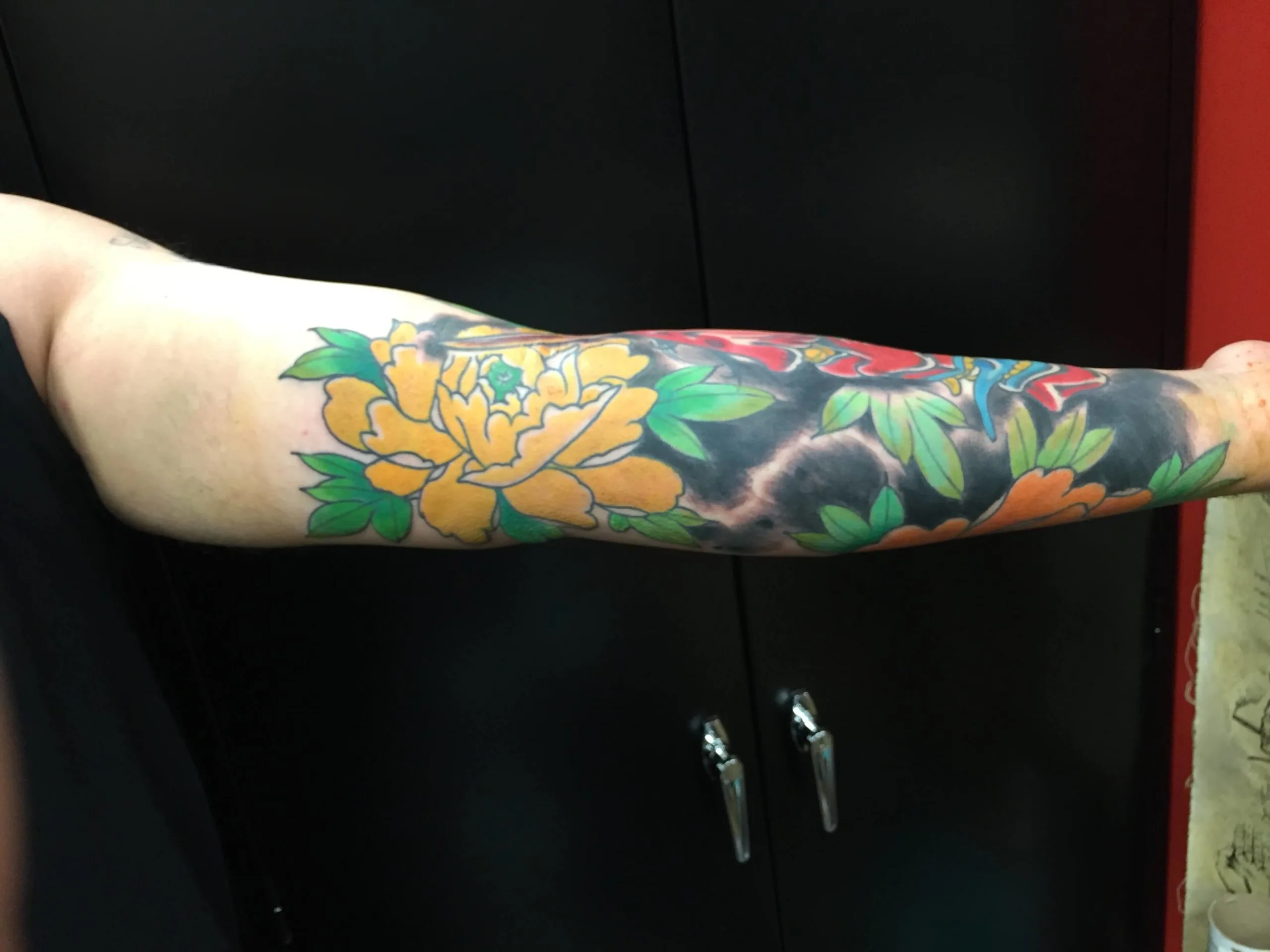 Yellow peony with green leaves on the forearm, partial red floral accent and dark mottled shading