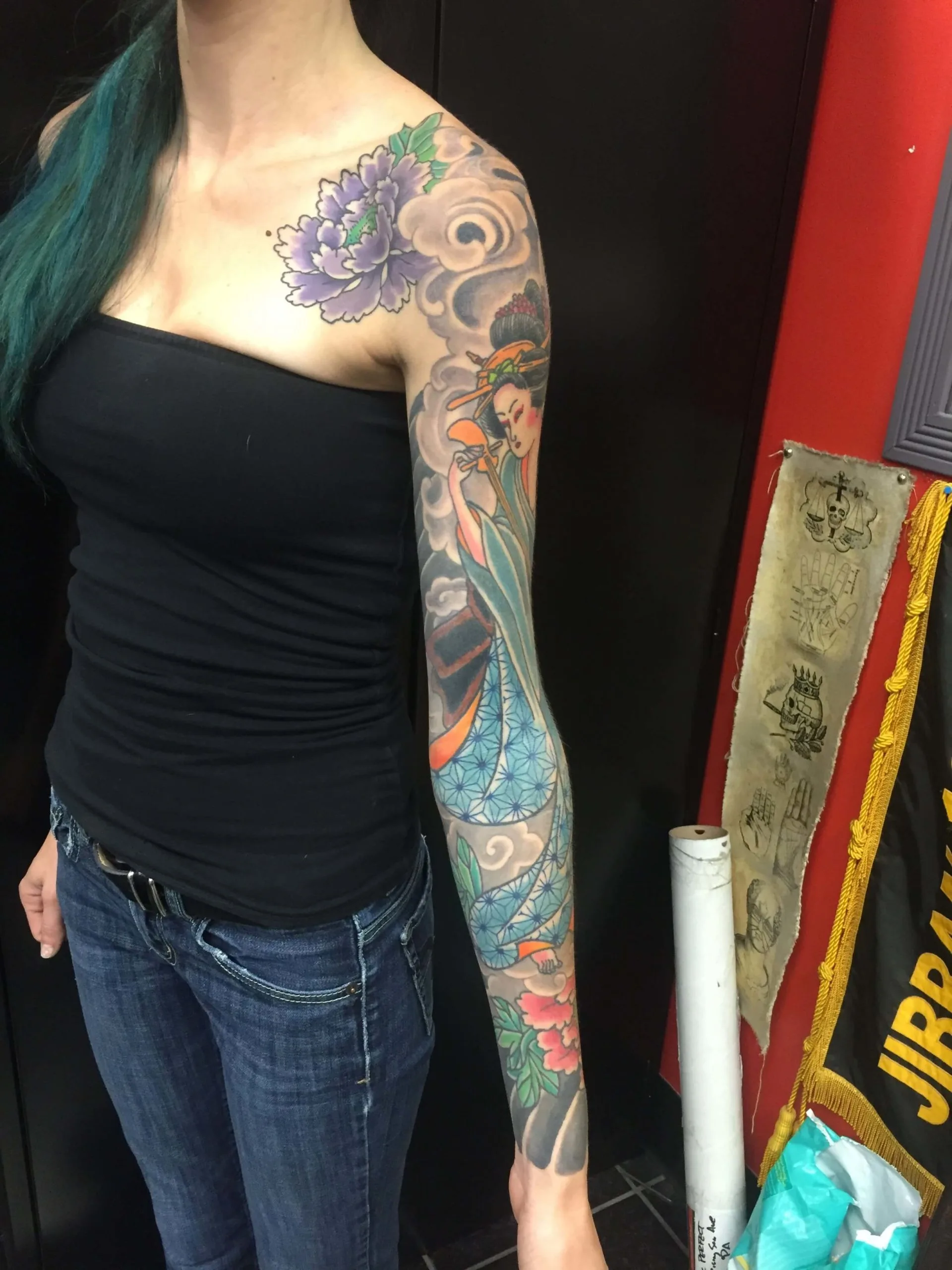 colour full sleeve with a purple peony at the shoulder, a blue-robed figure on the upper arm, and pink flowers near the wrist