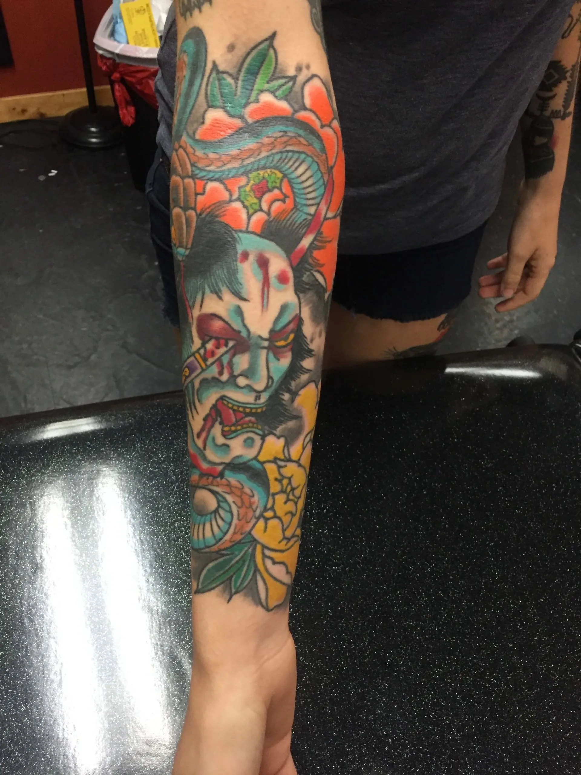 Red hannya mask with blue detailing and yellow chrysanthemums on the forearm