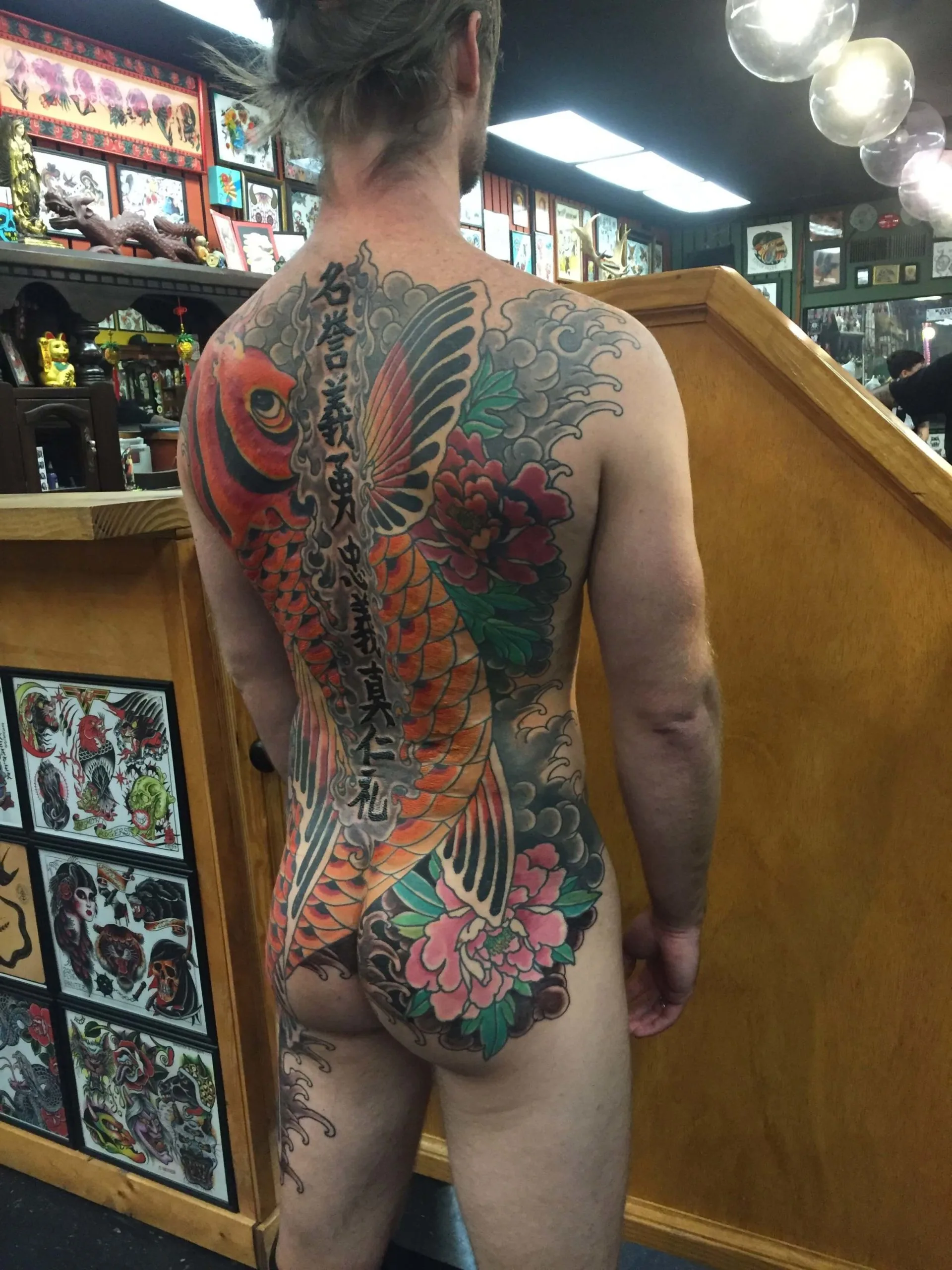 Colour full back piece of an orange-red koi fish with vertical kanji lettering and pink peonies below