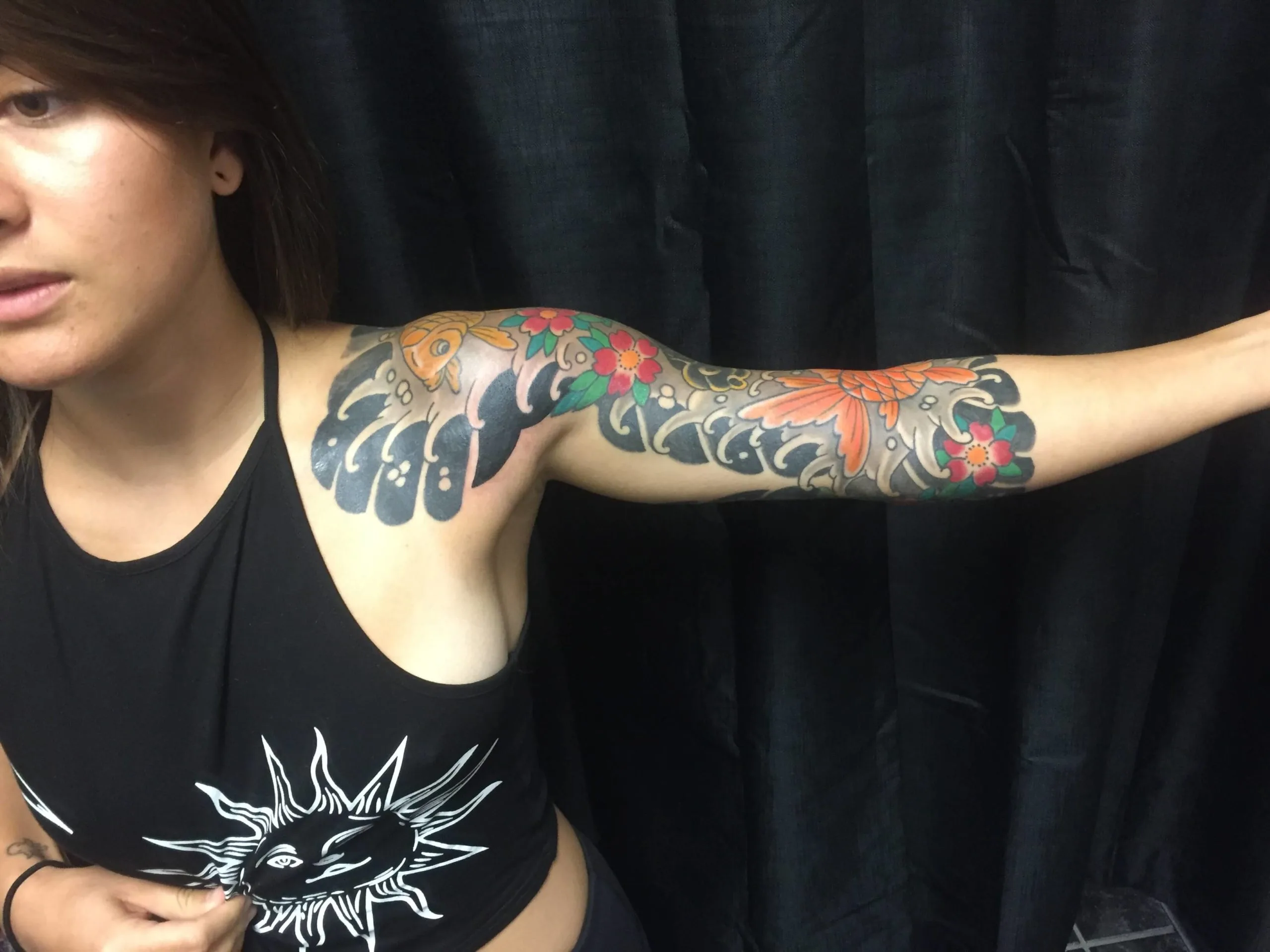 Shoulder and upper arm with an orange koi fish, black wave patterns, and red and green flowers in colour