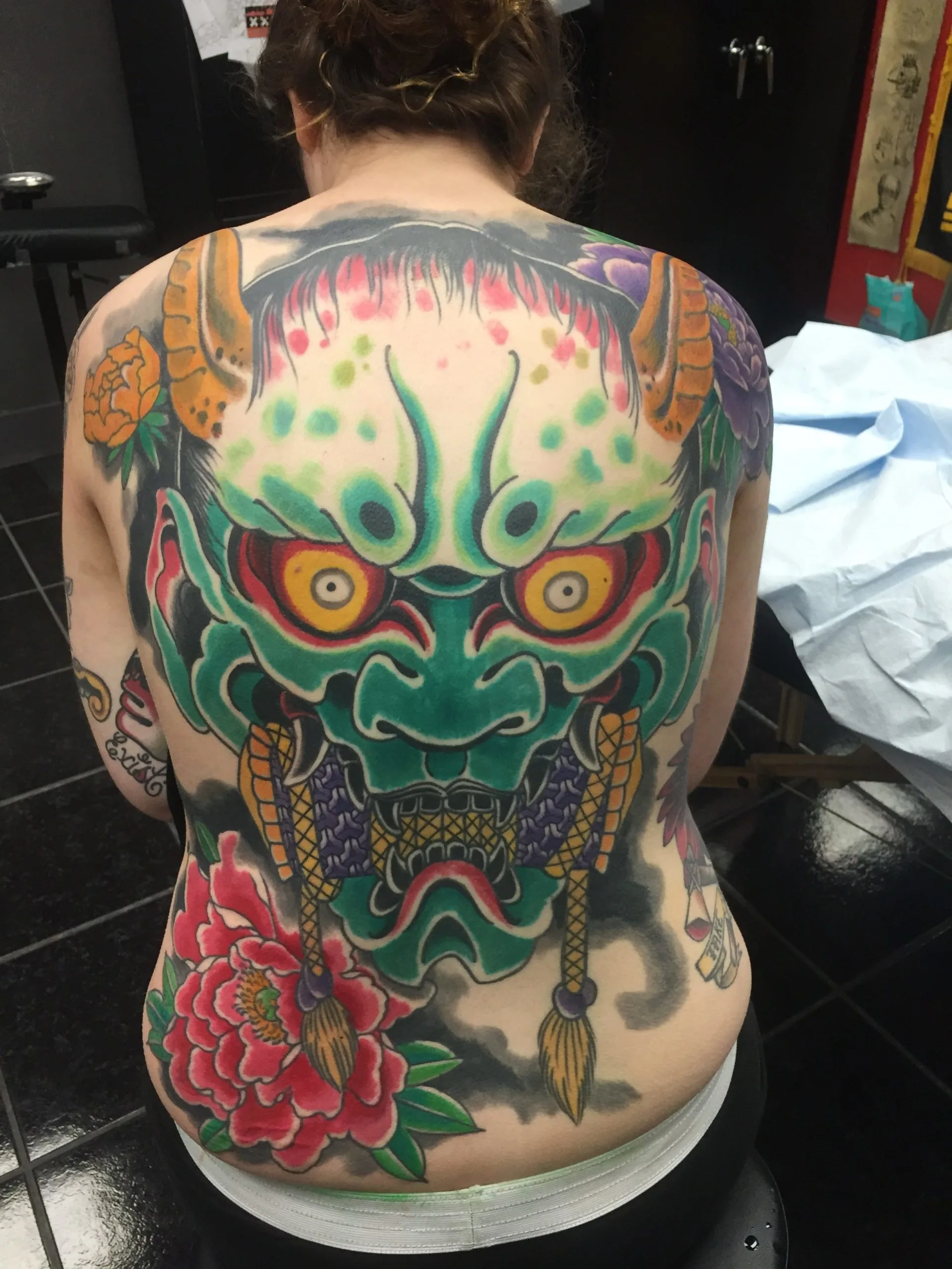 Full back piece with a green horned demon mask and peonies in red, orange, and purple