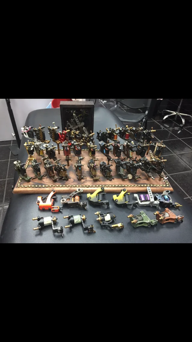 Collection of tattoo machines displayed on a wooden rack with additional machines lined up on a chair