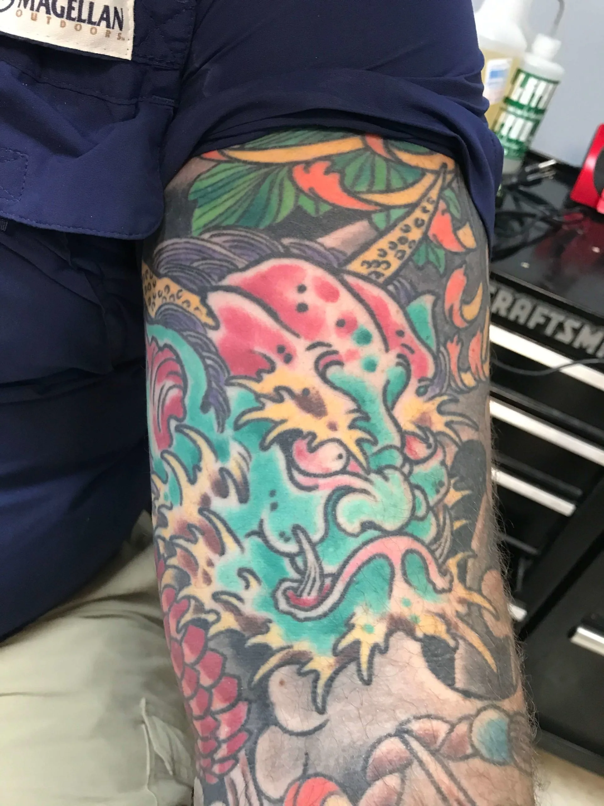 Color upper arm tattoo of a teal oni-style mask with red markings and orange flame details