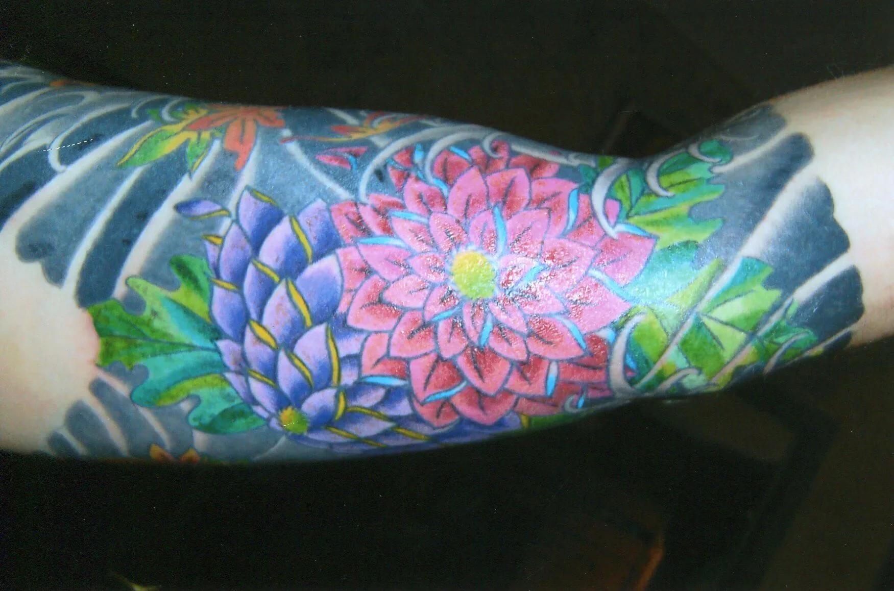 Close-up of a color arm tattoo with layered pink and purple flower blossoms
