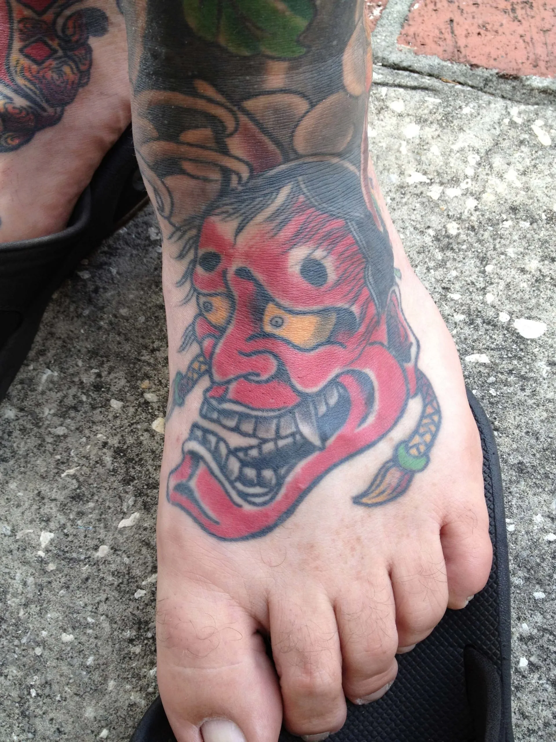 Red hannya mask with grey hair and a small dagger tattooed on top of the foot