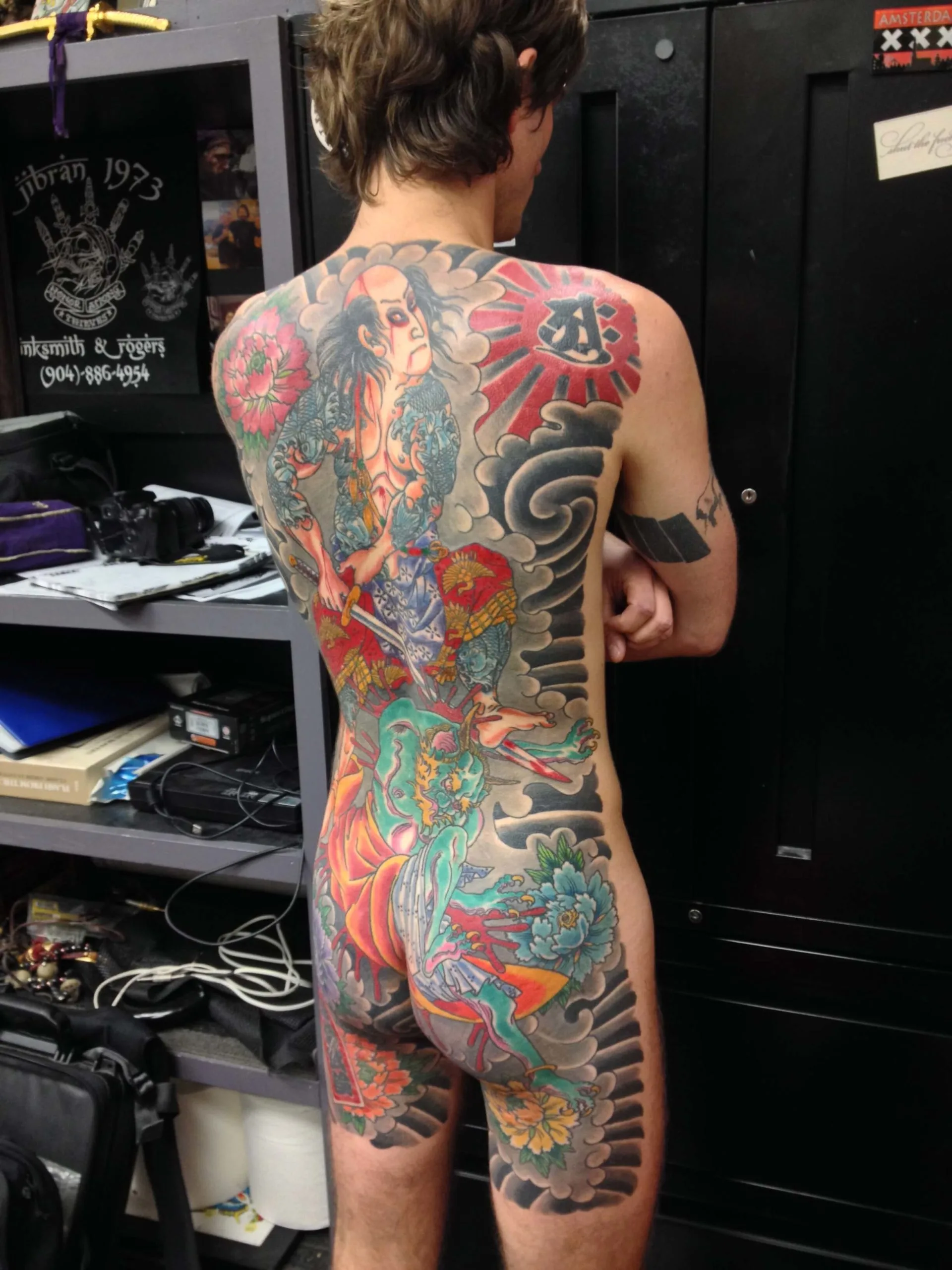 Full back piece with a robed figure holding a blade, a red sun, and a grey cloud and wave border