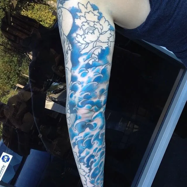 Leg sleeve with an uncolored peony outline above a shaded blue wave design, in progress