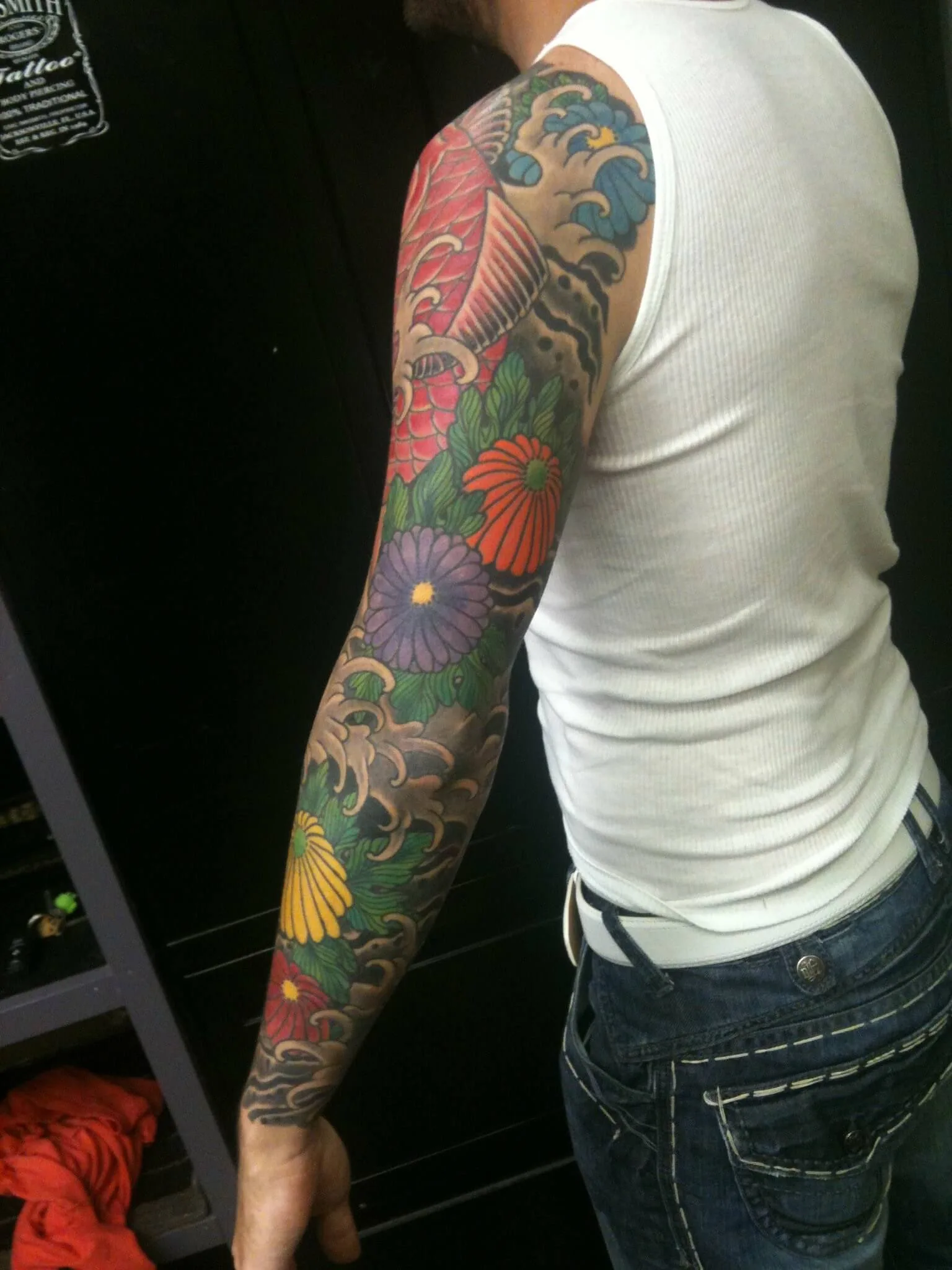 Full arm sleeve with orange, purple and yellow chrysanthemums, green leaves and a wave crest