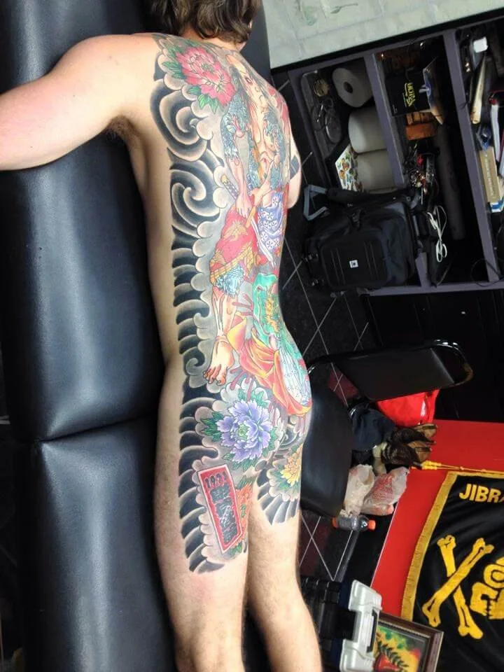 Full back piece with a robed figure, grey wave borders, and pink and blue peonies