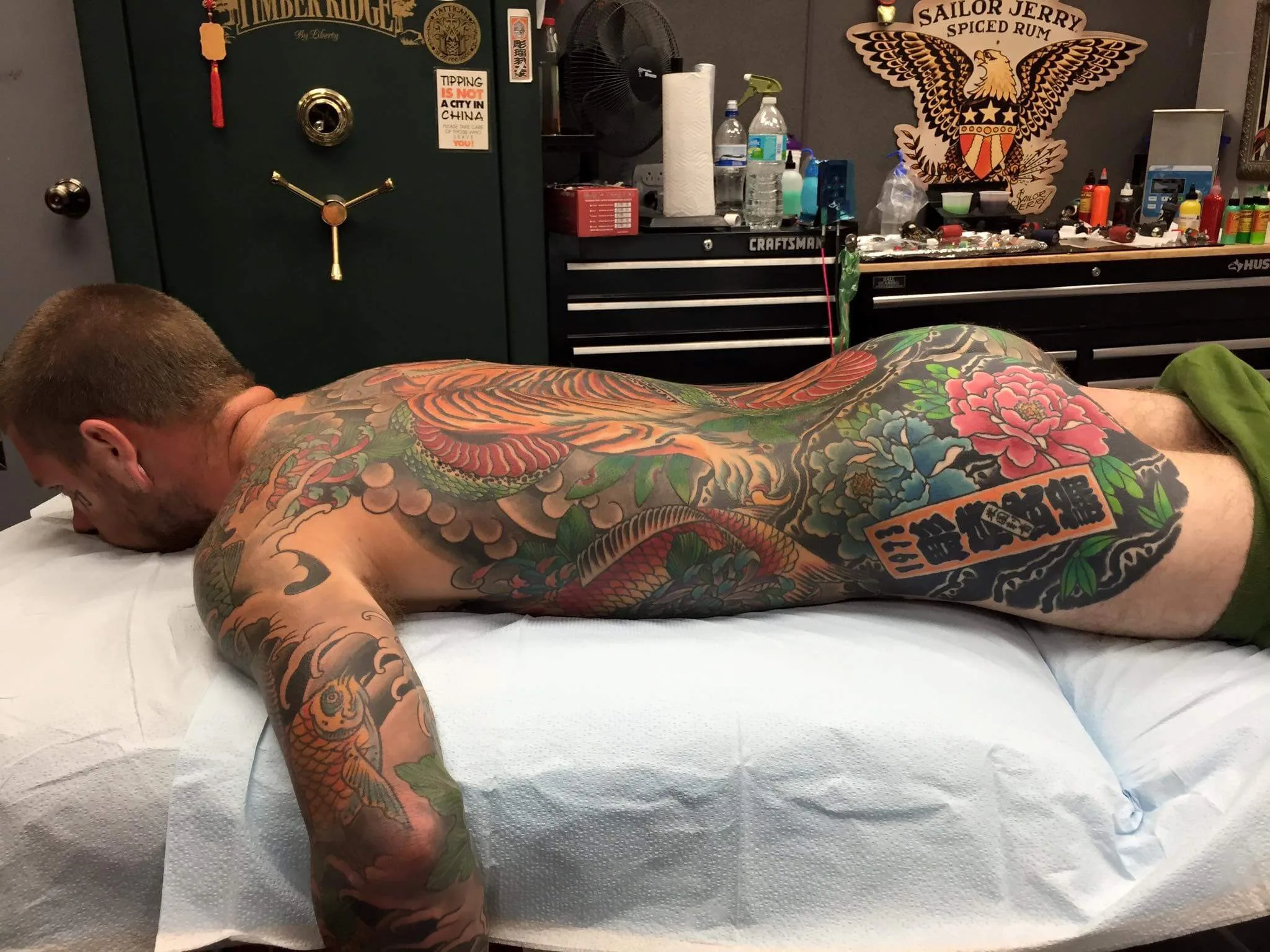 Full back piece with a large orange and green scaled creature amid clouds, koi visible on the forearm