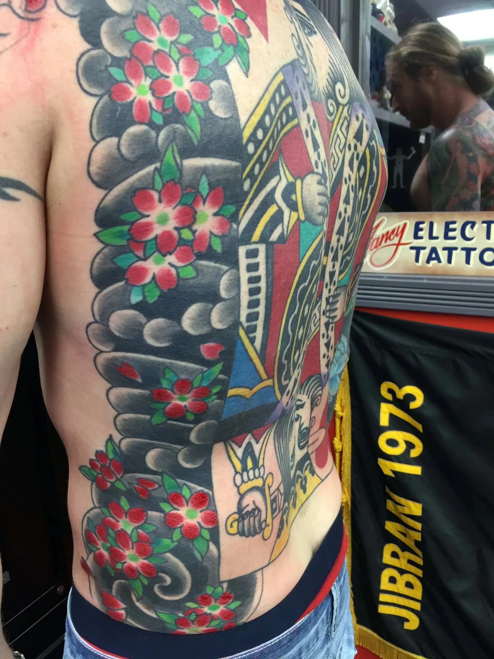 Colour back and side piece of a large playing-card king figure, framed by red cherry blossoms and grey scalloped clouds