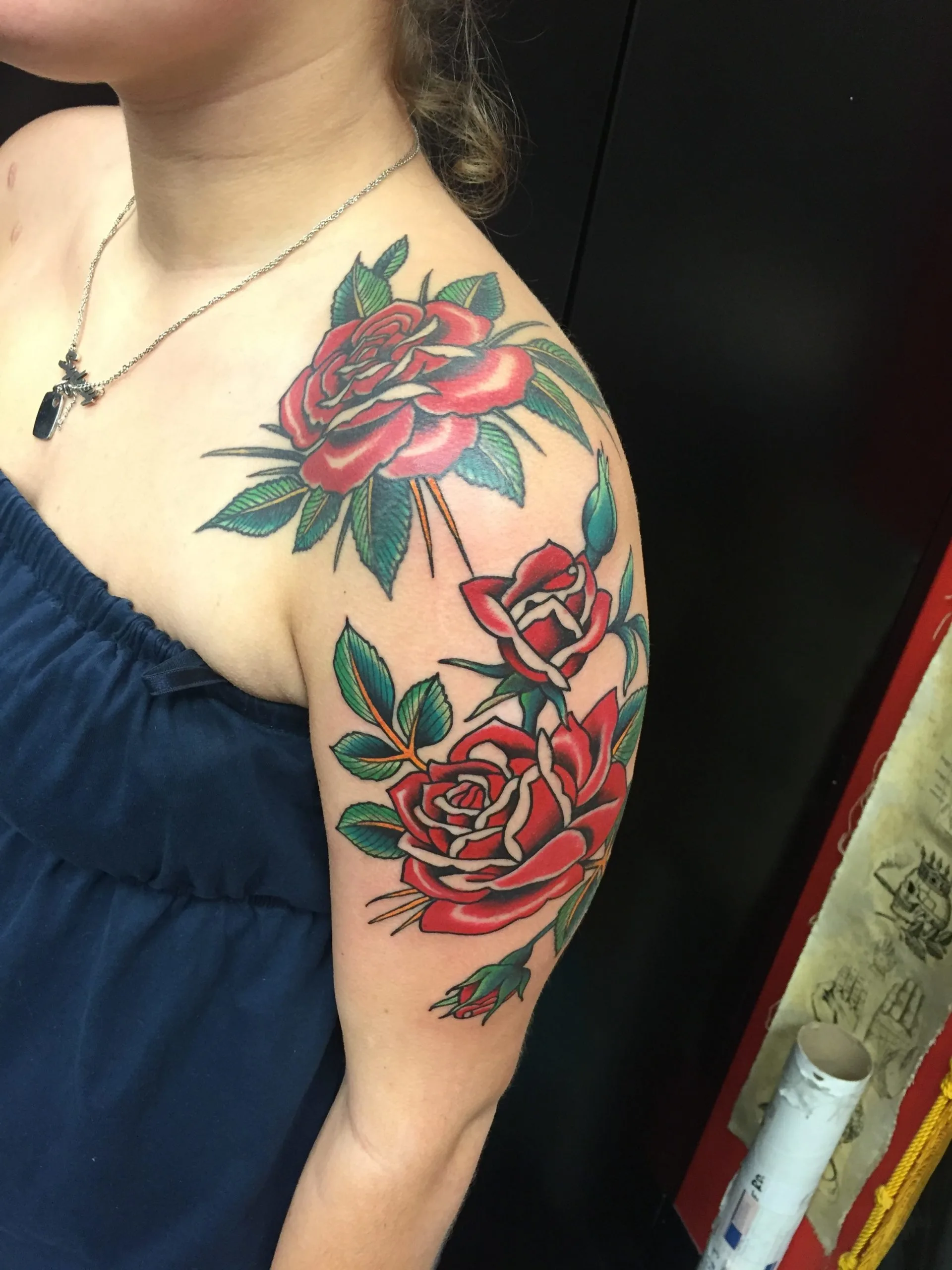 Color tattoo of three red roses with green leaves across the shoulder and upper arm