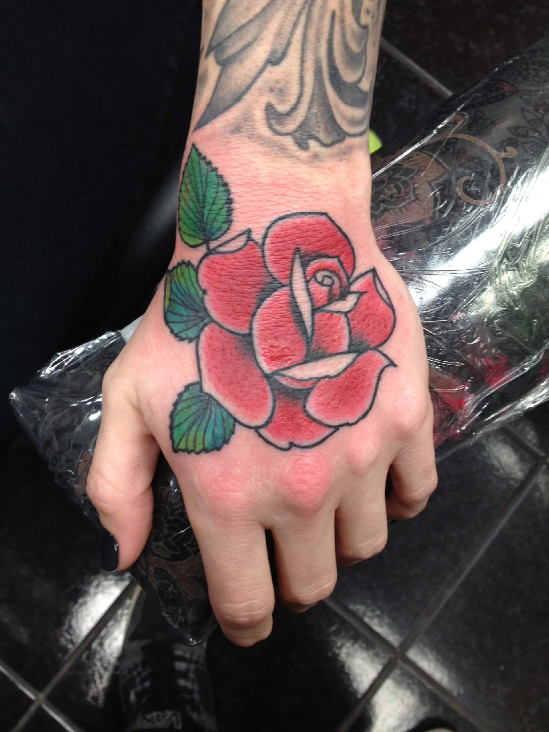 Red rose with green leaves on the back of the hand