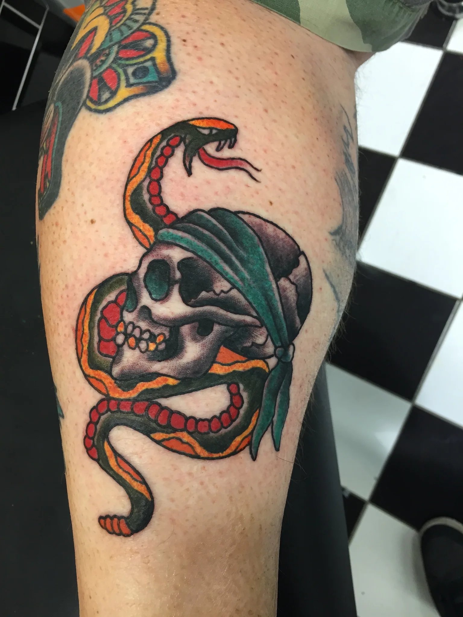Colour thigh tattoo of a snake coiled around a skull wearing a green bandana