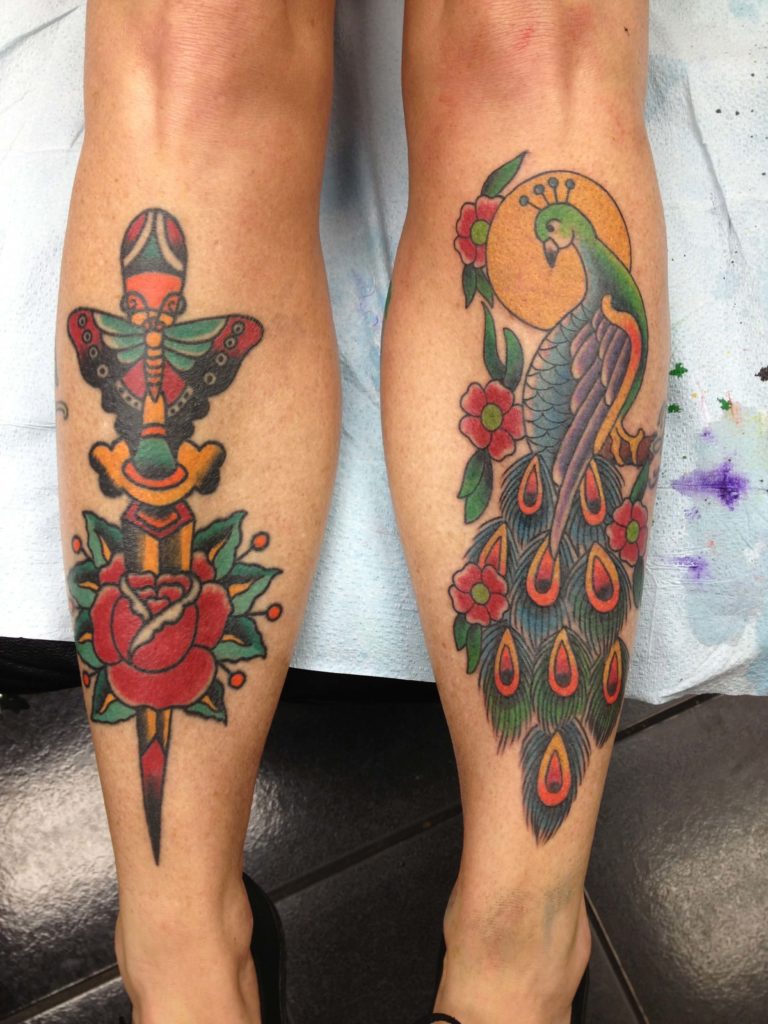Both lower legs: left with a dagger through a moth design above a red rose, right with a peacock and red flowers