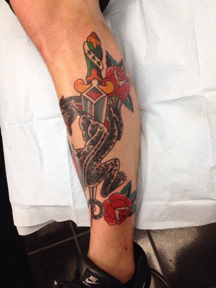 Snake wrapped around a dagger with a heart accent and roses on both sides, on the calf