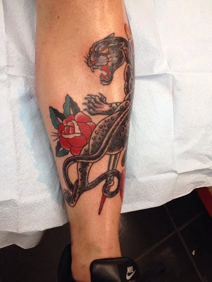Lower leg with a black panther, a red rose, and a curling black tail shape below, in colour
